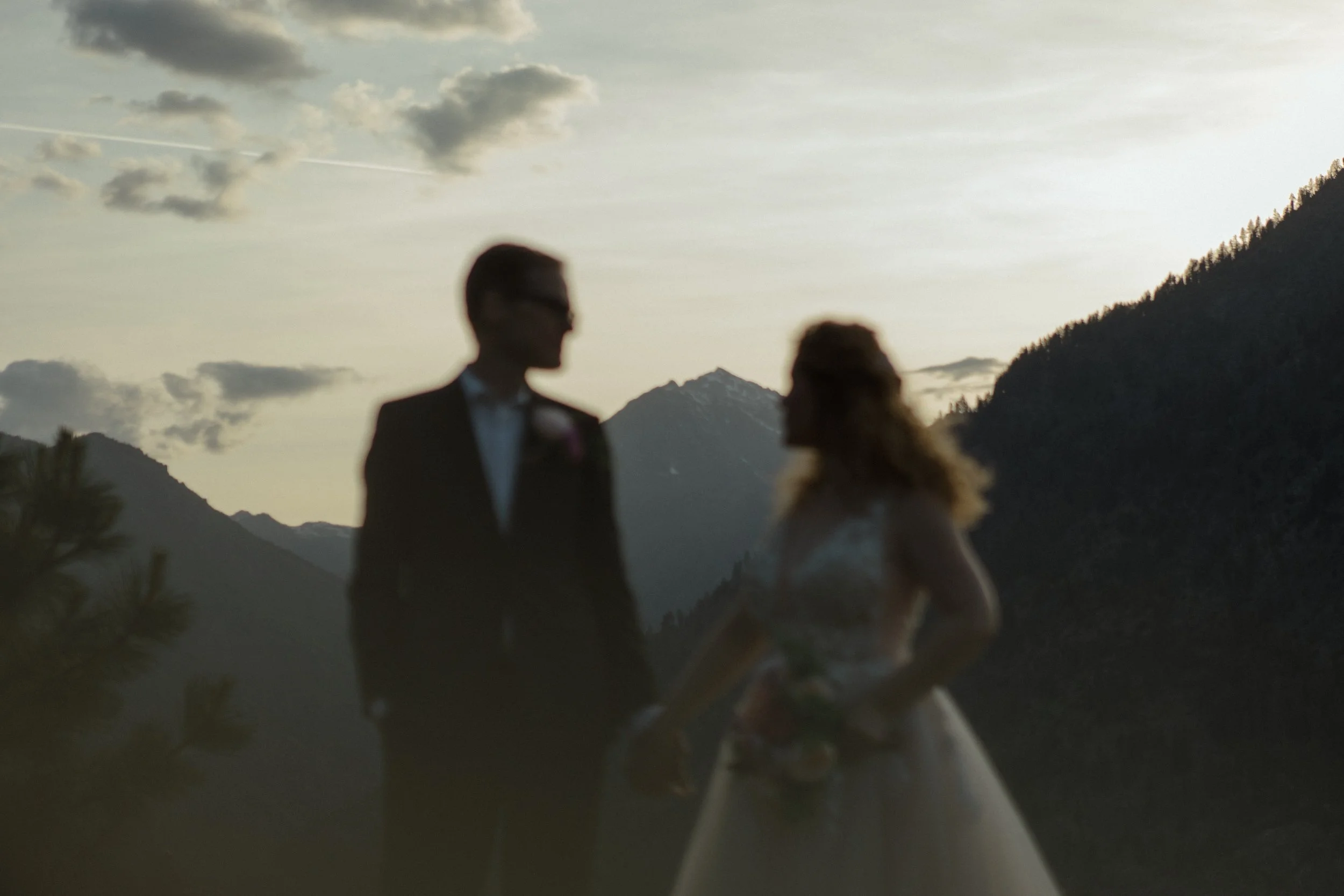 The bride and groom stand out of focus with the Enchantments in focus in the background at sunset in Leavenworth above the town.