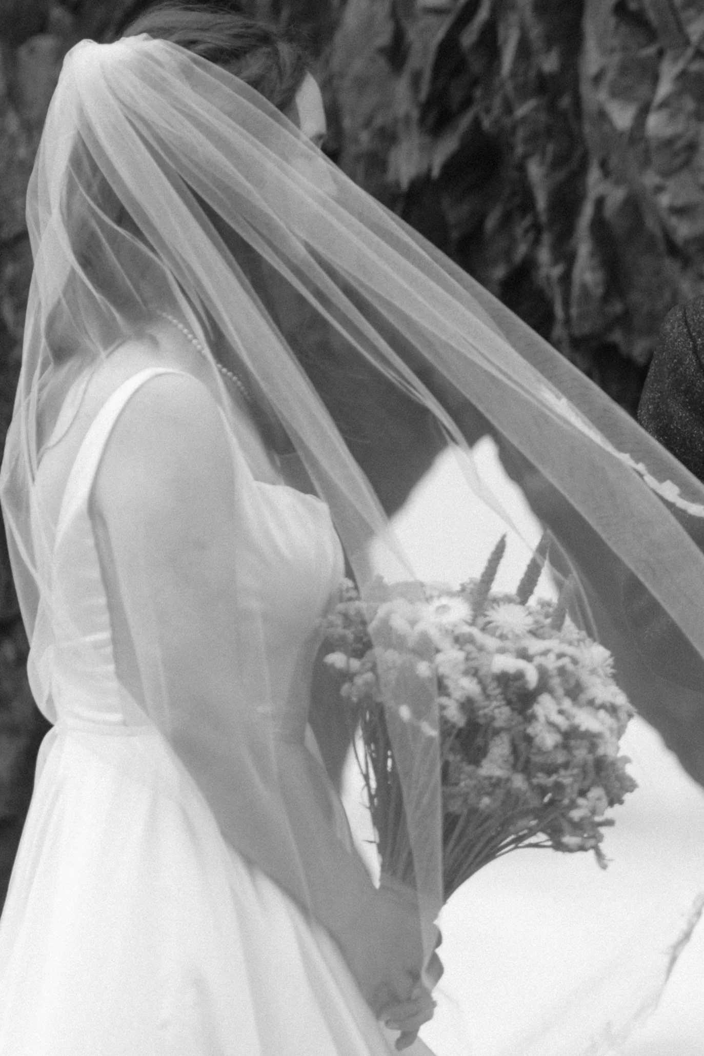 A bride stands at the rock alter at Ruby Beach holding her flowers in an artistic black and white photo.