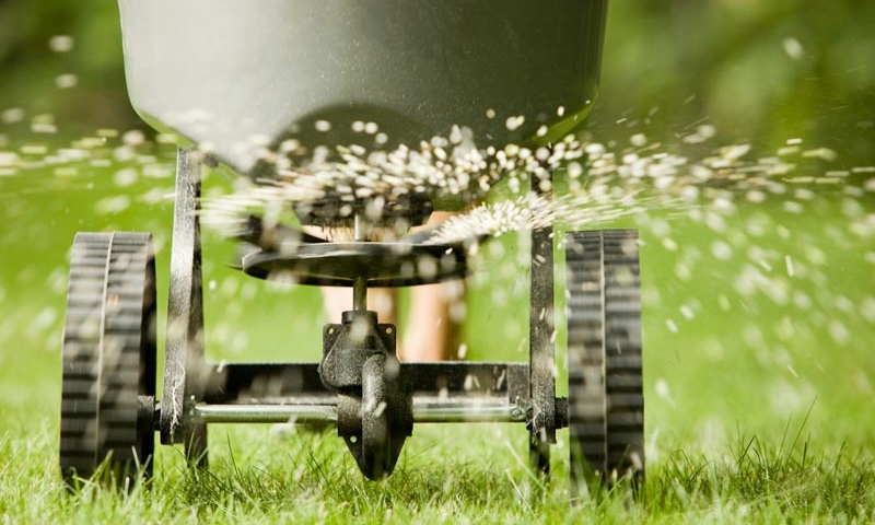 Hand pushed fertilization cart spewing seeds onto lawn, part of complete lawn maintenance by Ivanoff.