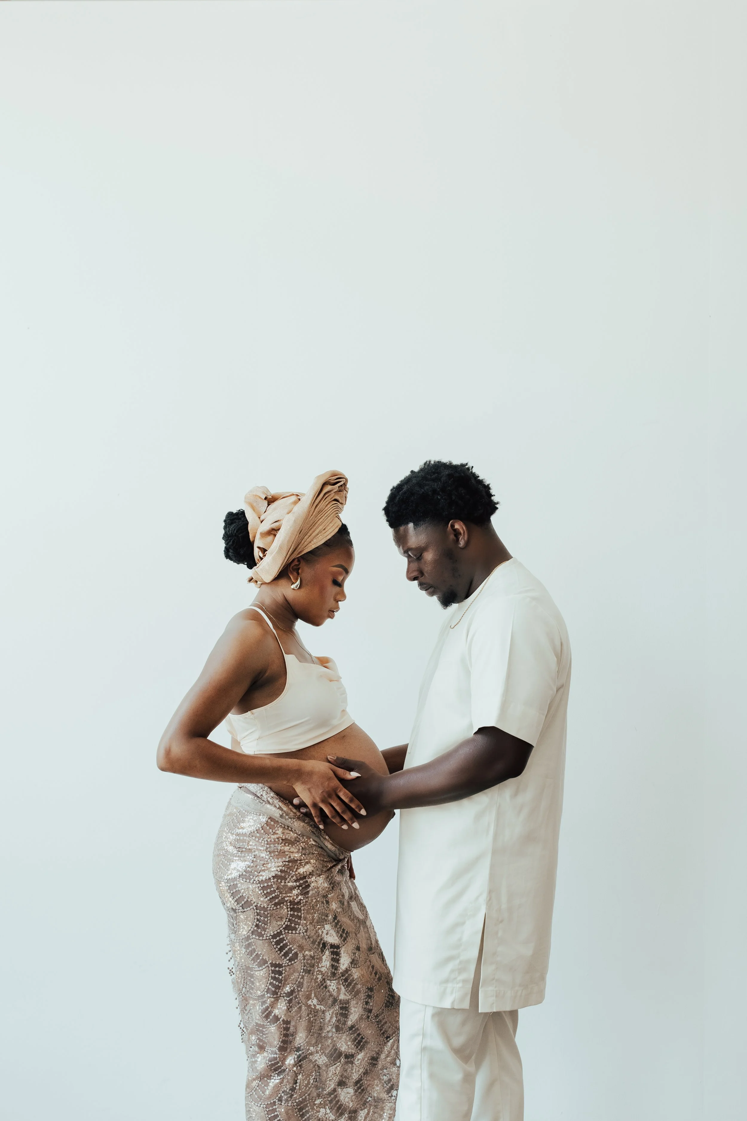 A pregnant woman and a man are gently touching her belly, with their heads bowed and eyes closed, against a plain light background. Dallas Fort Worth DFW Texas Maternity Photographer