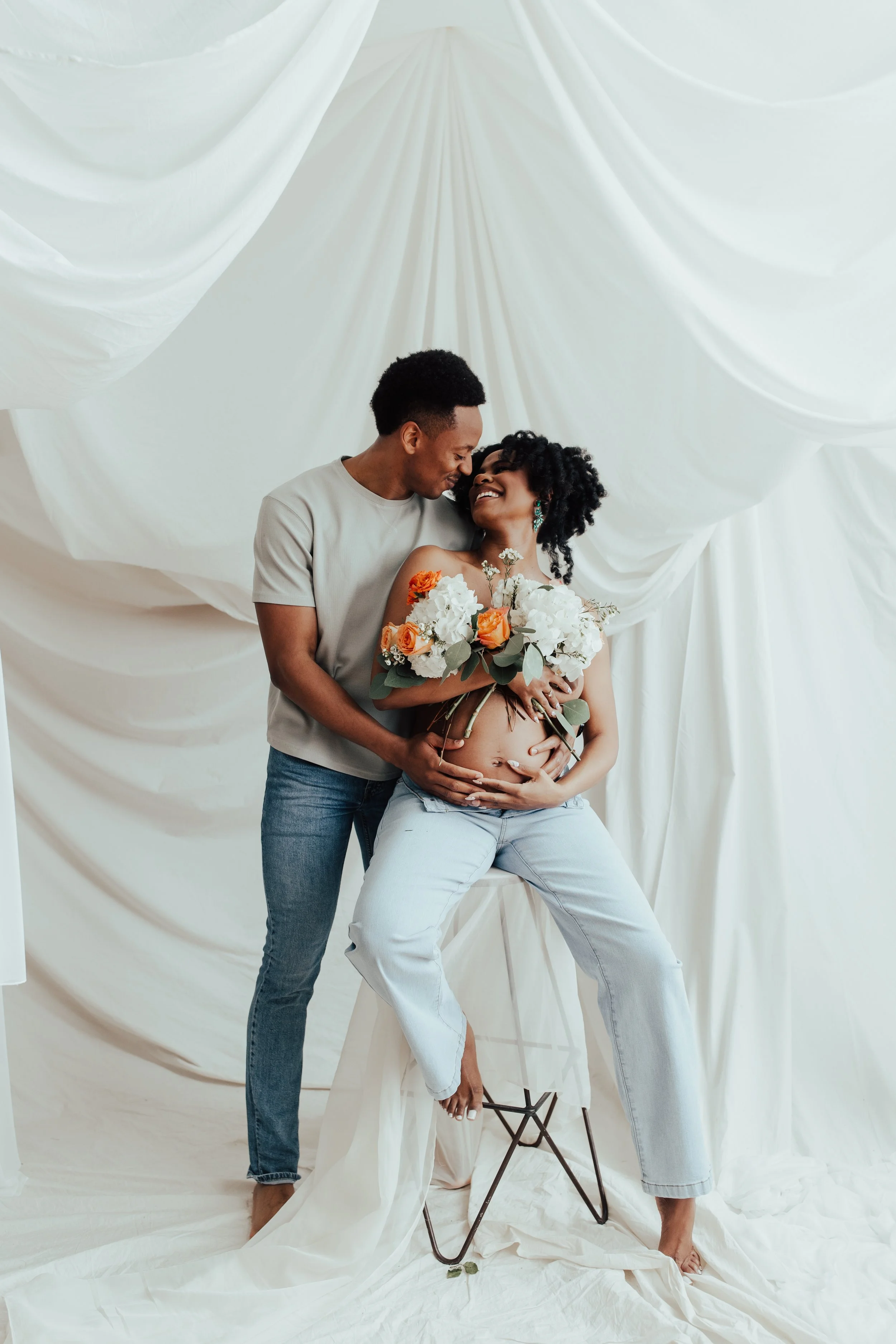A pregnant woman and a man are posing together in front of a white draped backdrop. Dallas Fort Worth DFW Texas Maternity Photographer