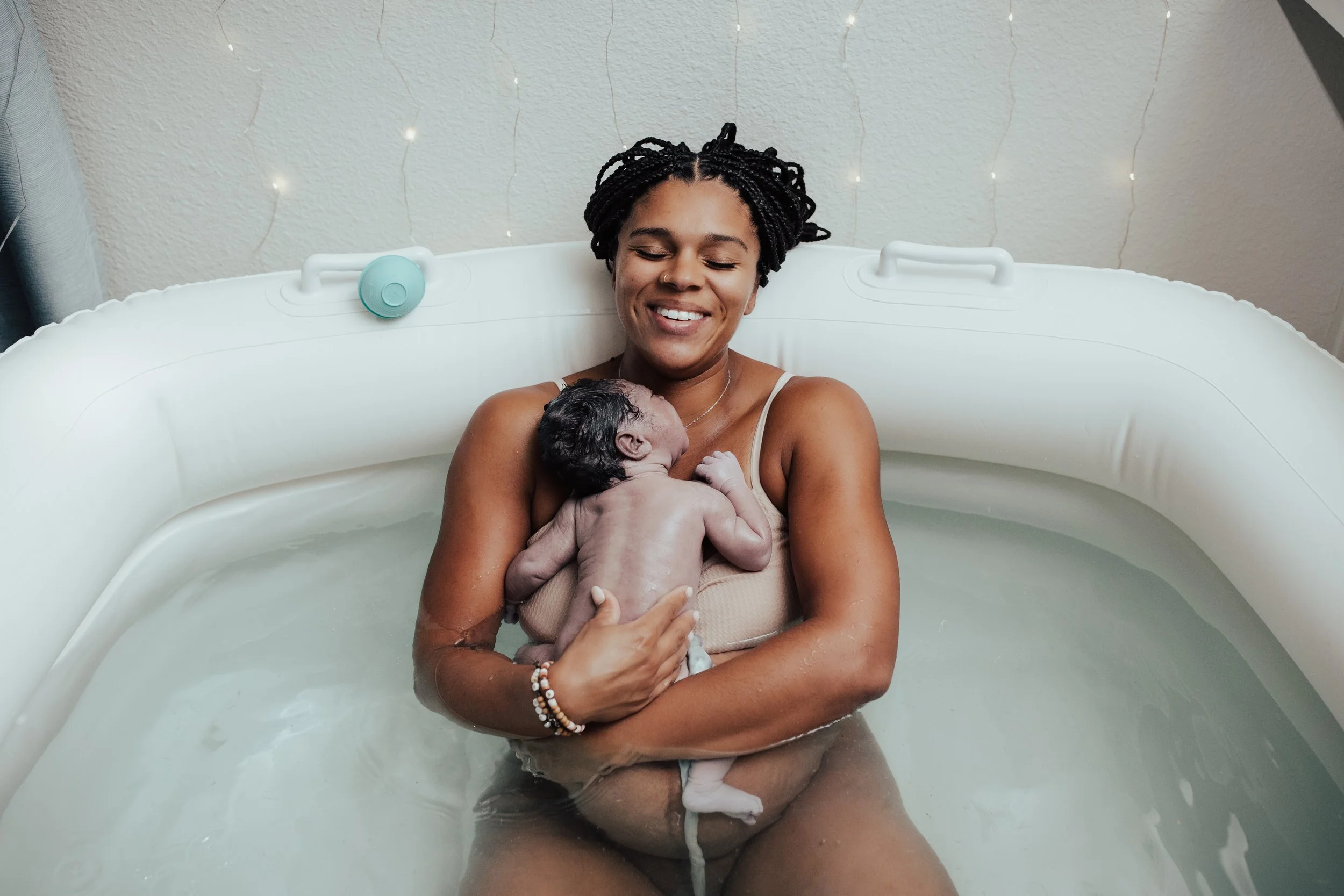 A woman in a birth pool holding a newborn baby close to her chest, smiling with closed eyes in a peaceful moment. Dallas Fort Worth Maternity photoshoot Carmen Bridgewater photography