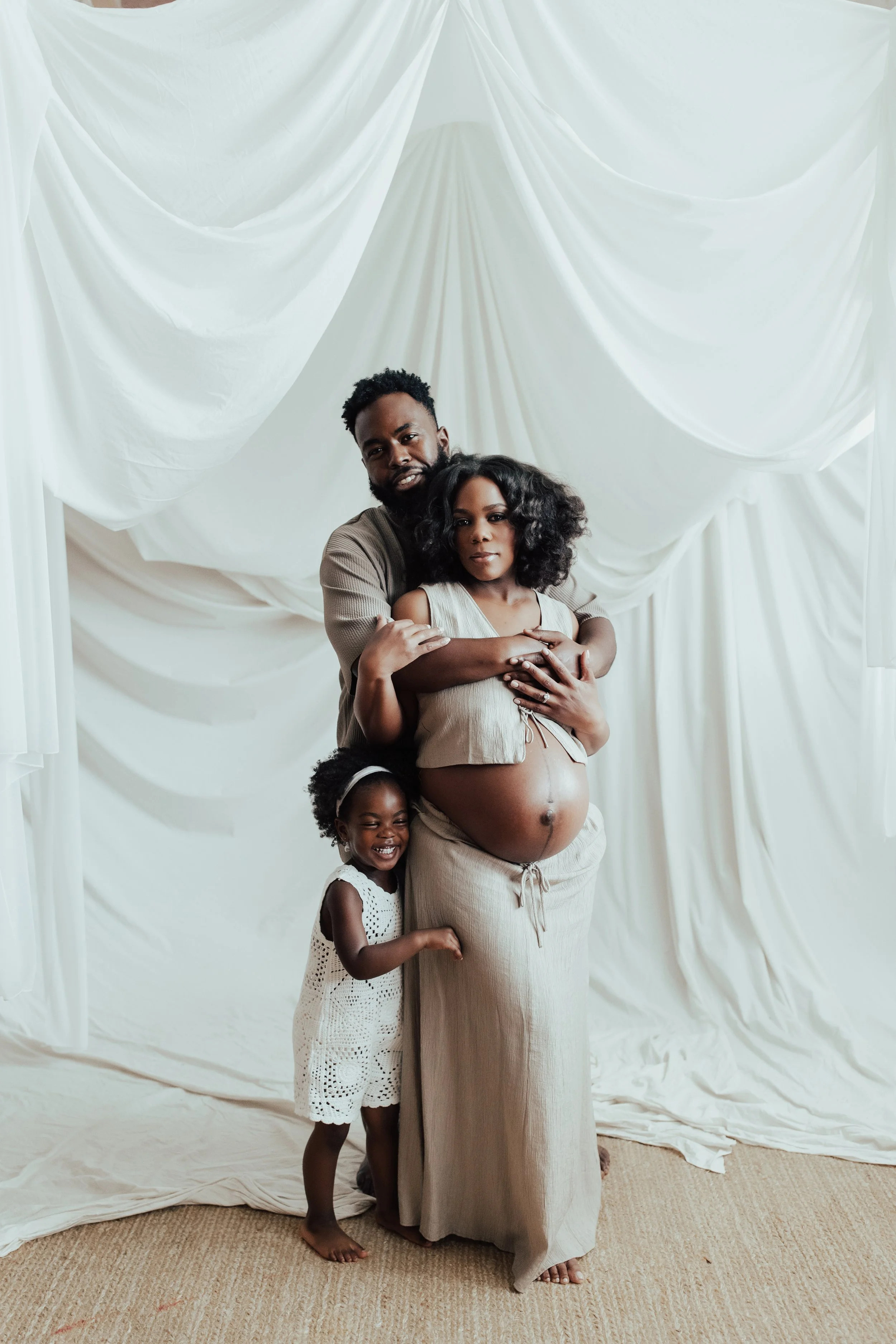 A family portrait featuring a pregnant mother with her children and partner, standing in front of white draped fabric. Dallas Fort Worth DFW Texas Maternity Photographer