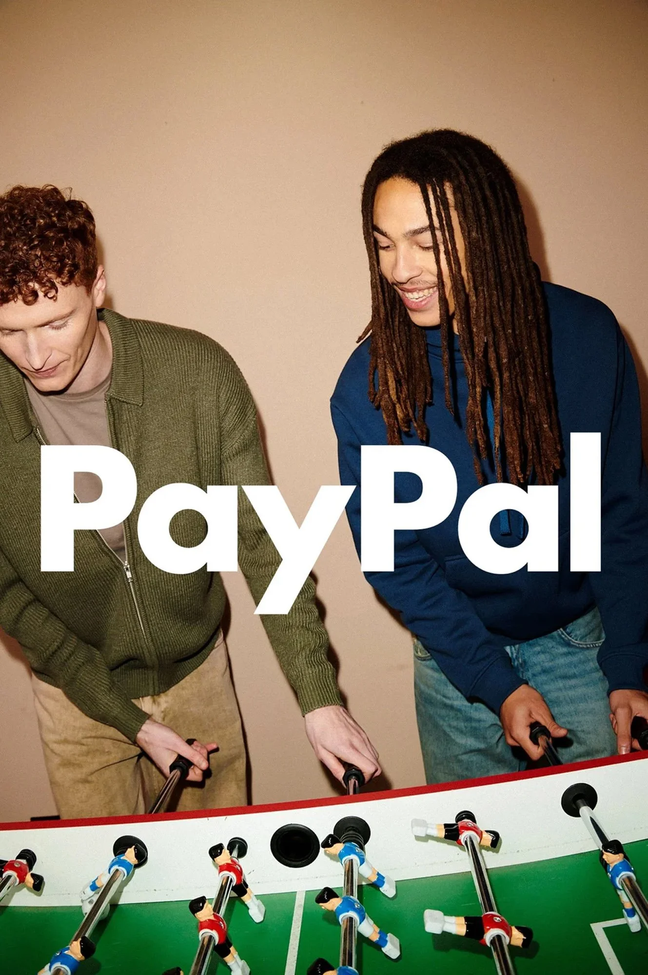 Two young men playing foosball with a PayPal logo overlay.