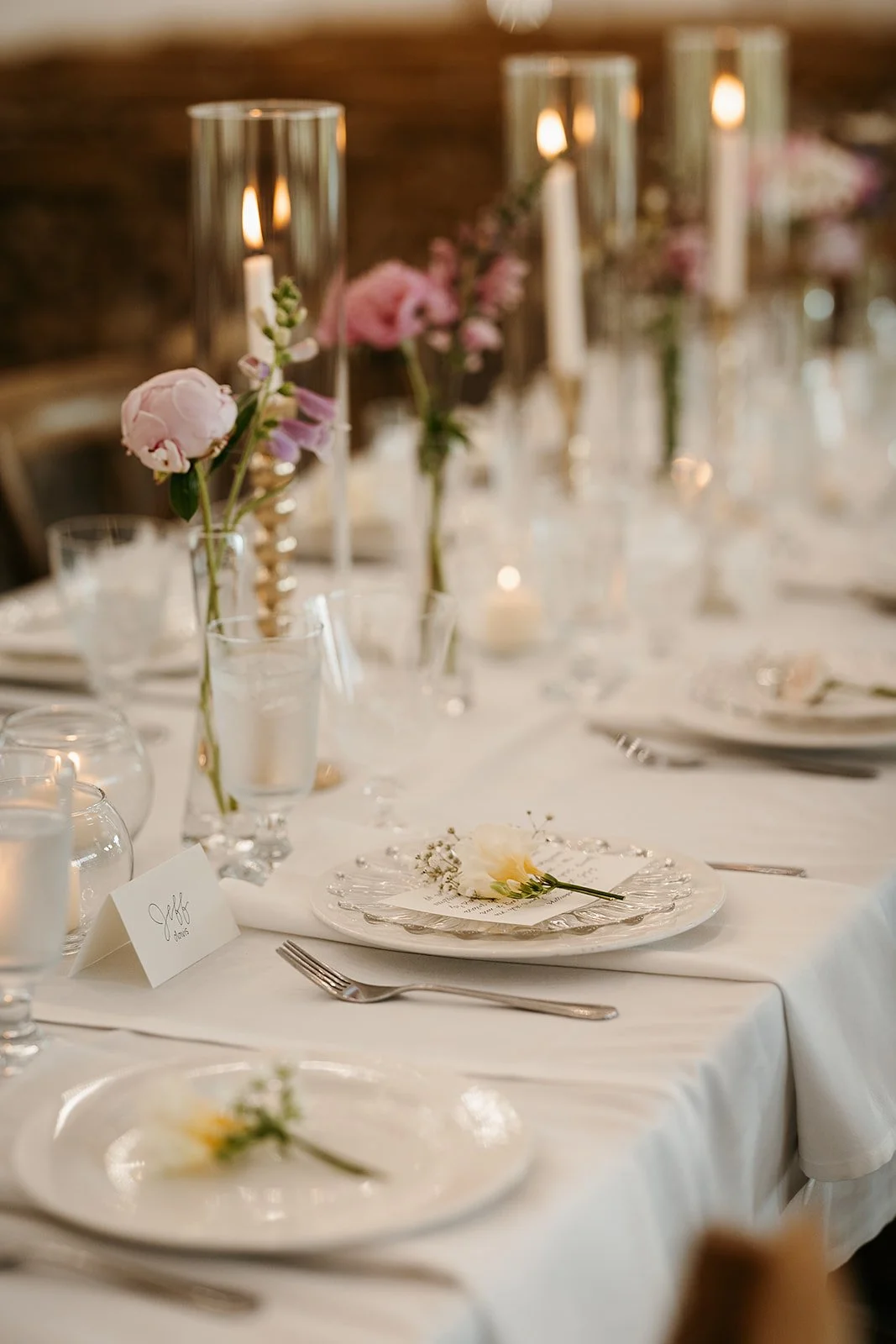 Elegant wedding reception table with floral centerpieces, candles, and place settings with a name card that reads 'Jeff'.