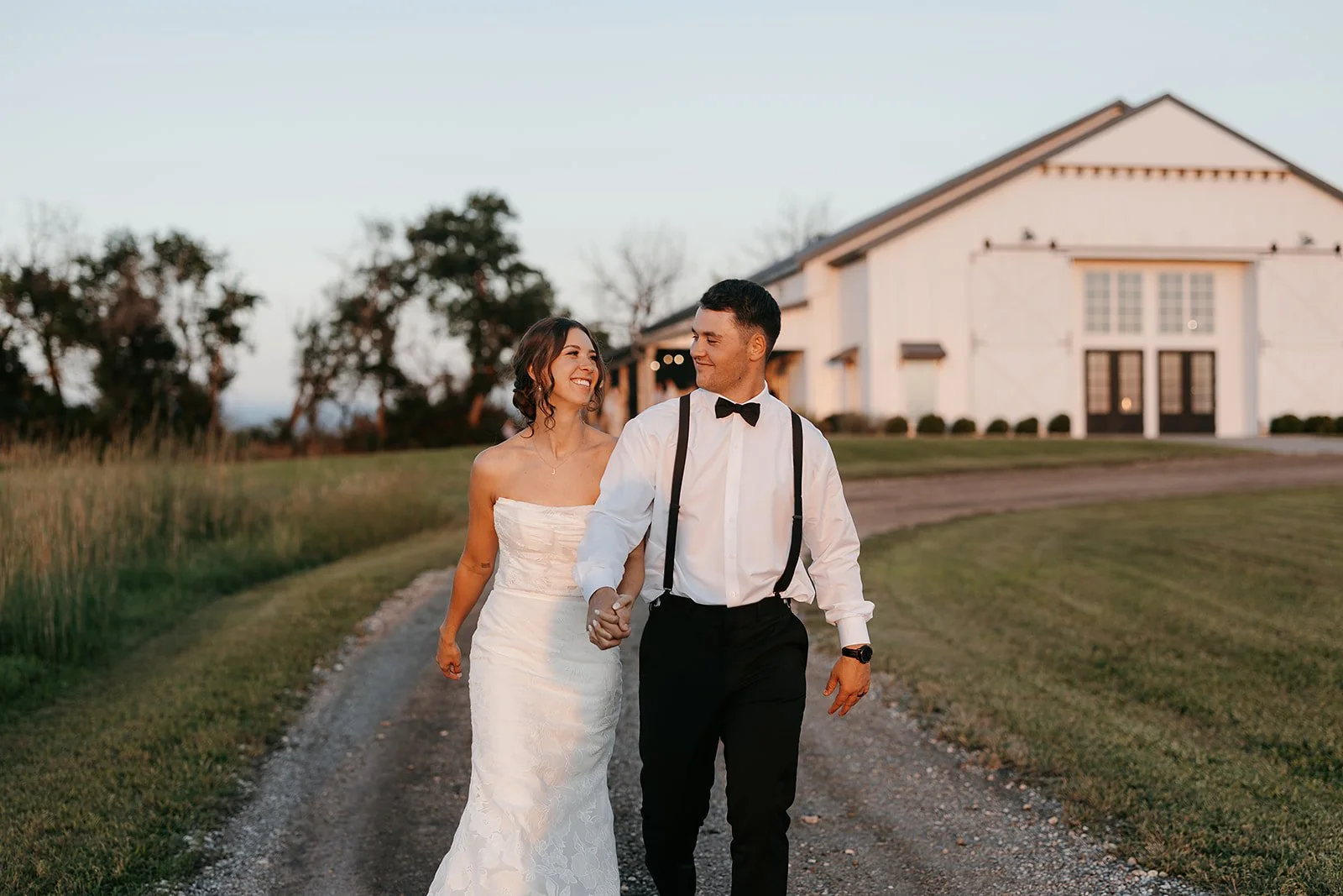 the new mr. and mrs. during sunset with the white barn venue behind them.