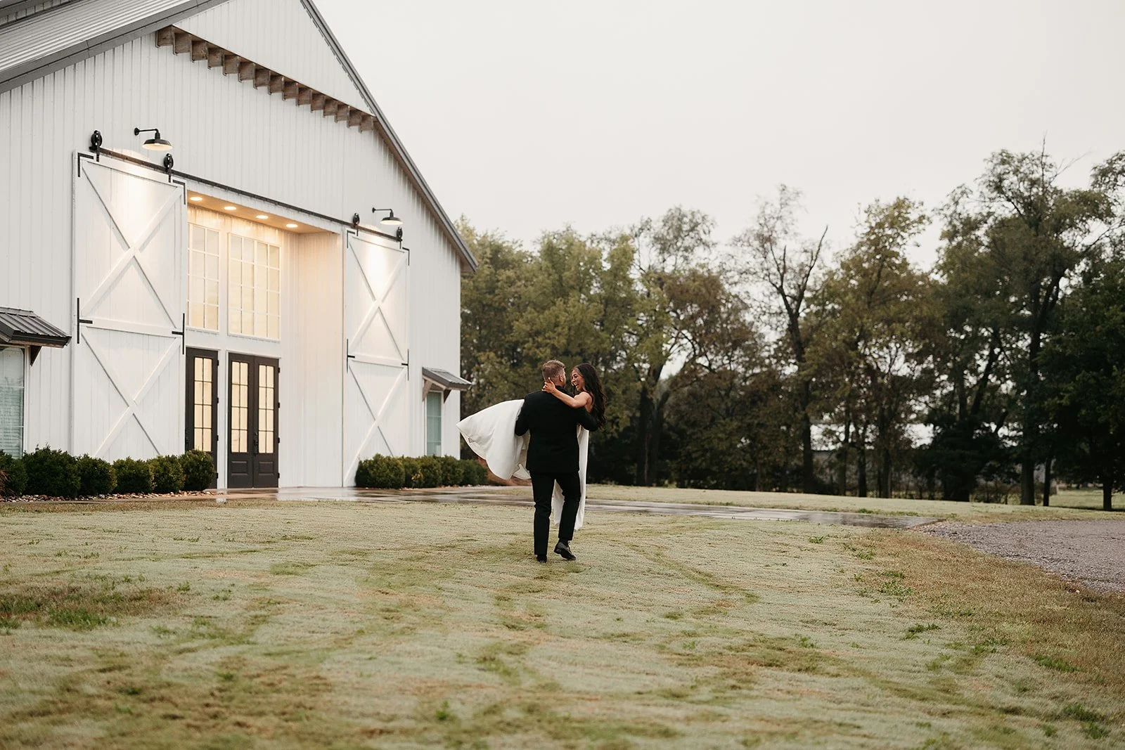 groom carrying bride in his arms in front of The Barn at Grace Hill