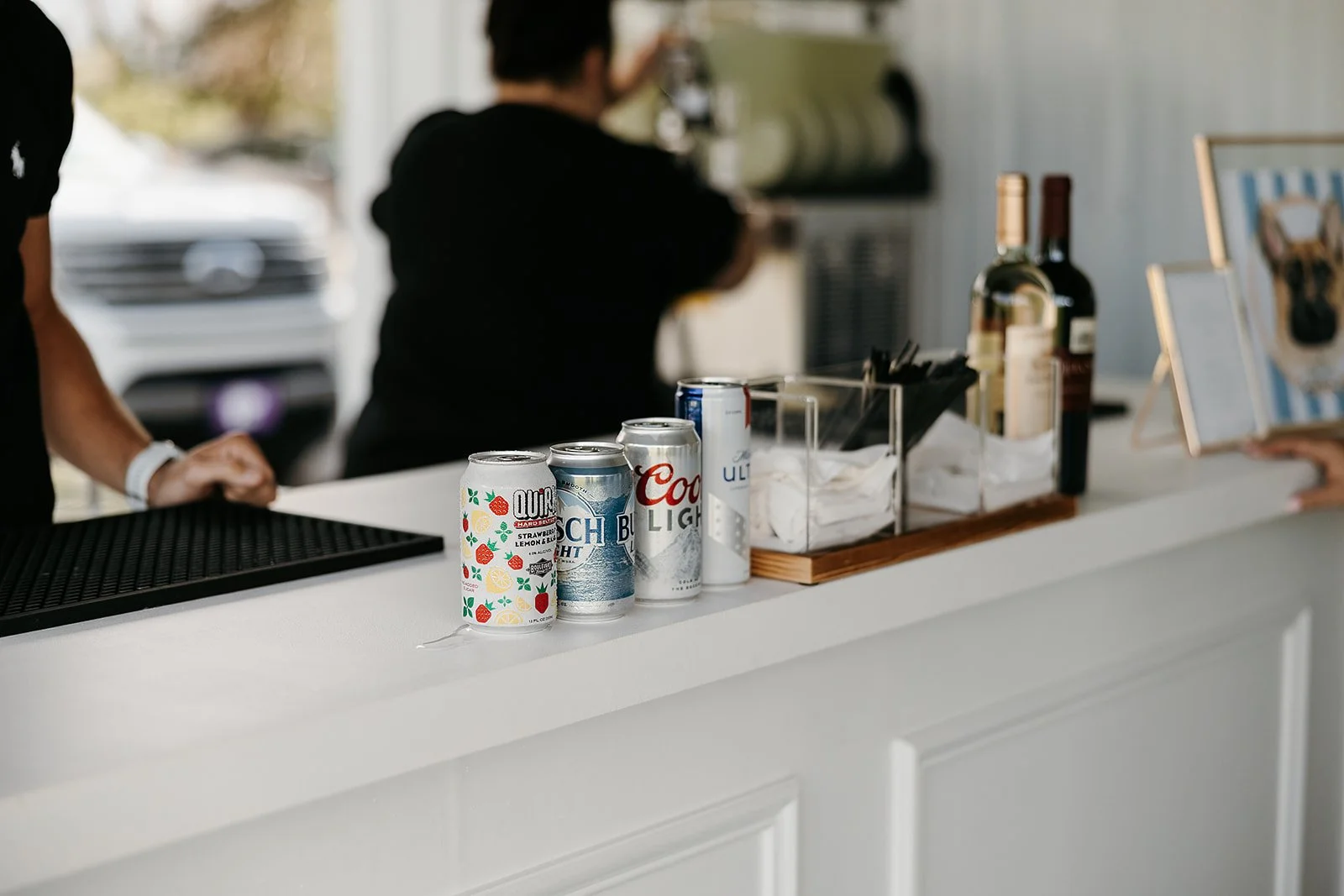 Counter with canned drinks, bottles of wine, and bar supplies at a bar or cafe.