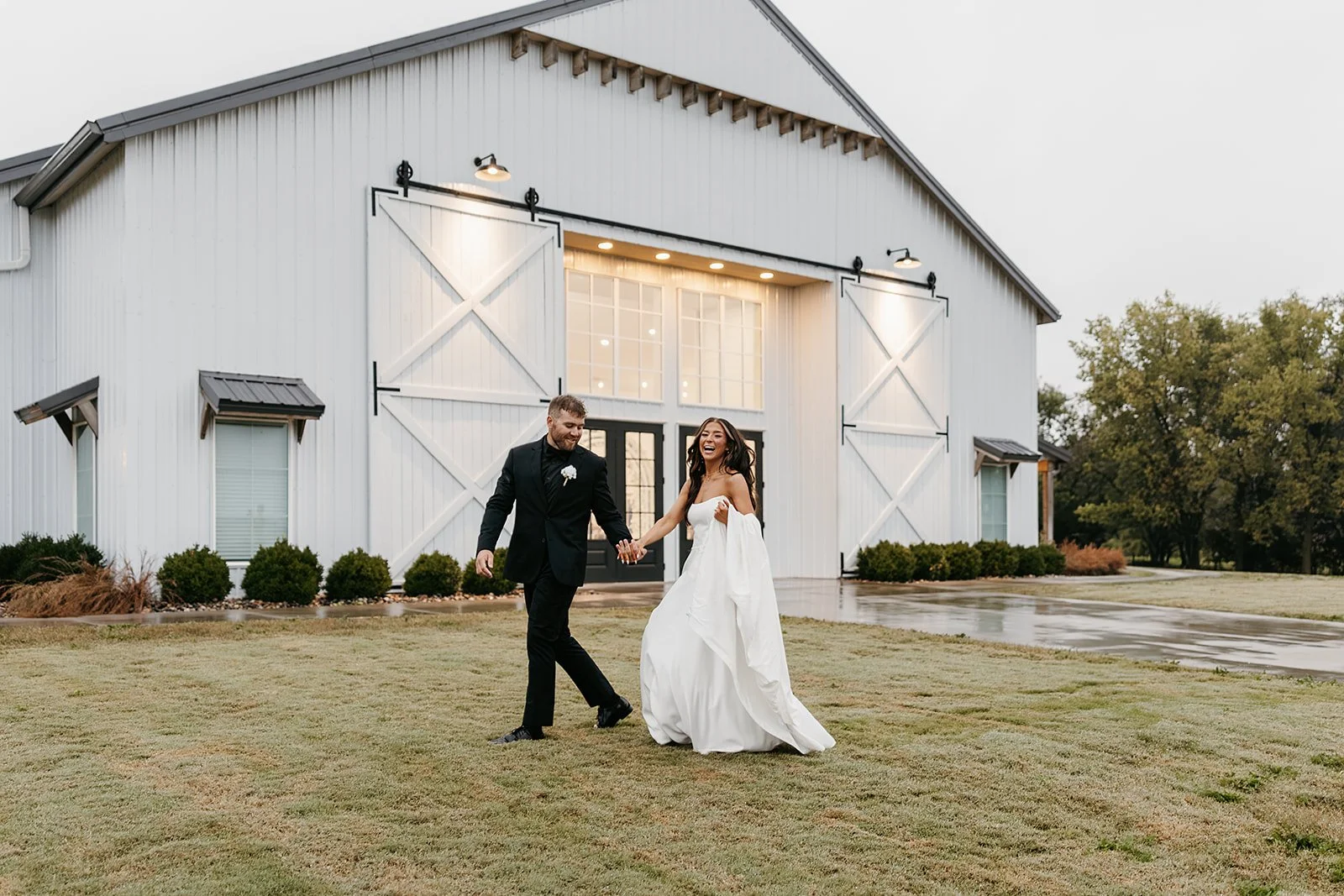 bride and groom on a rainy day in front of white barn wedding venue