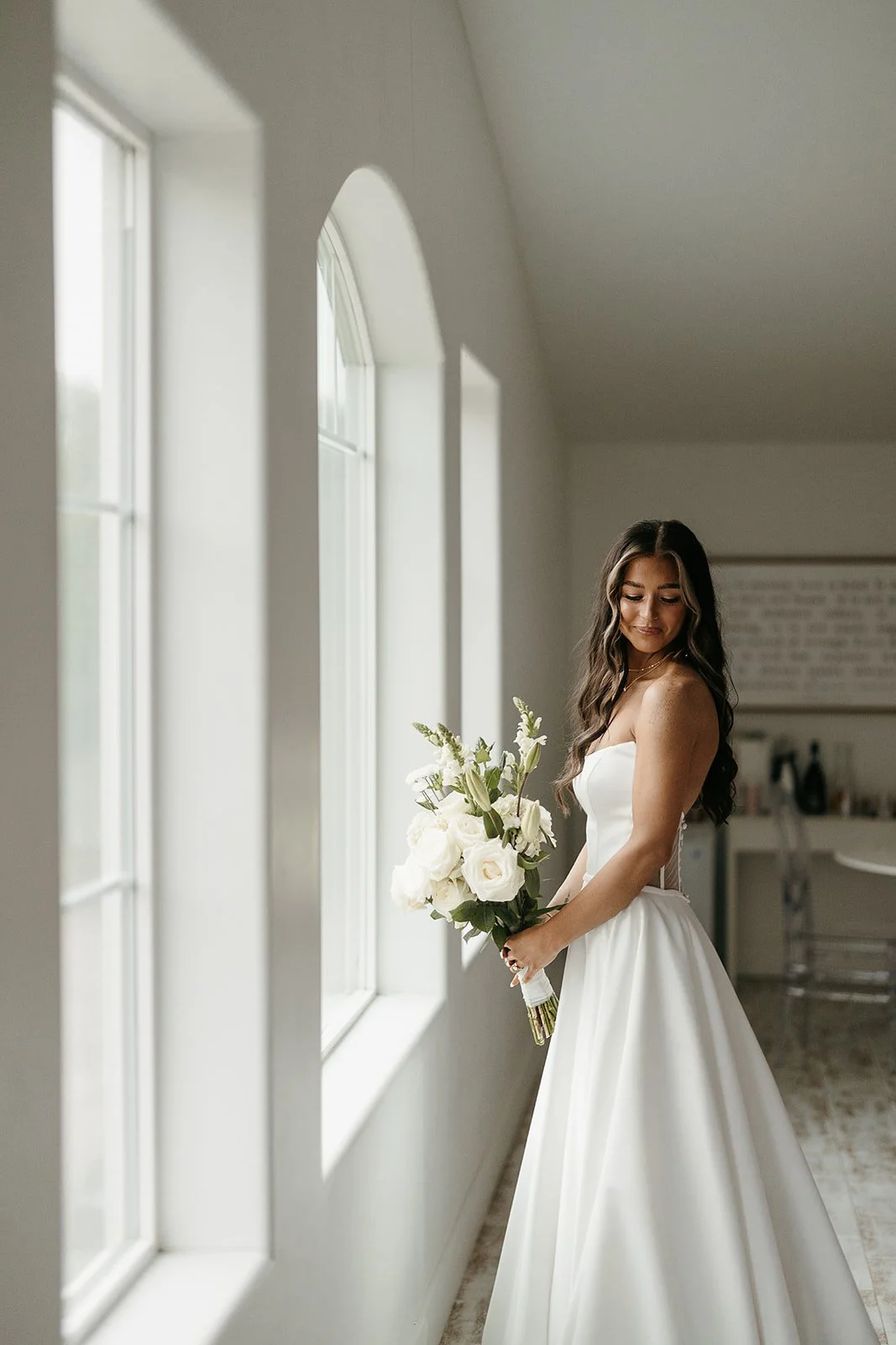 bride with bouquet standing next to arched windows