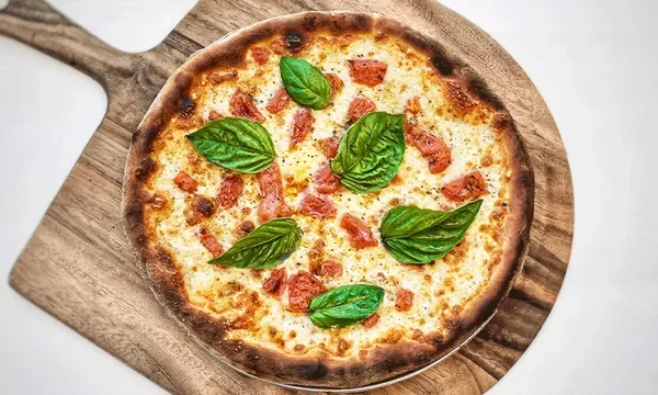Overhead shot of an Amici’s gluten-free Margherita pizza with fresh basil leaves on a wooden peel.