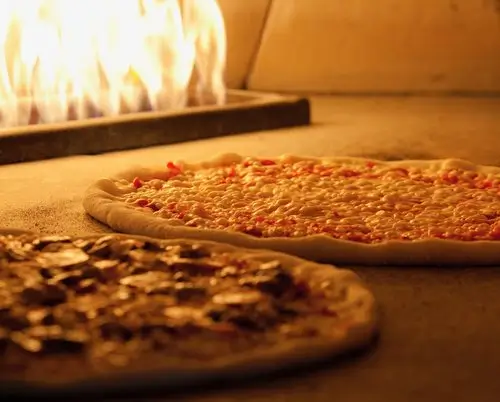 A vegan pizza topped with vegetables and Daiya cheese baking inside Amici’s pizza oven.