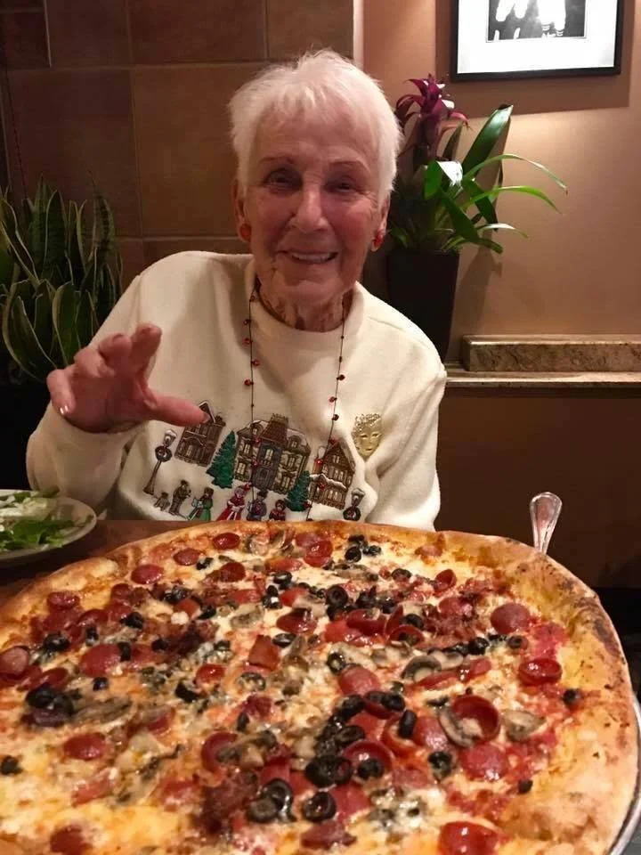 An older woman enjoying a large pizza at Amici’s East Coast Pizzeria.