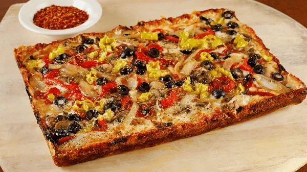 Amici’s Detroit-style Veggie vegetarian pizza with a bowl of chili flakes.
