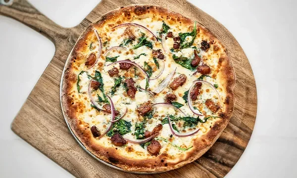 Overhead view of an Amici's Trentino gluten-free pizza with spinach, red onion, and bacon bits.