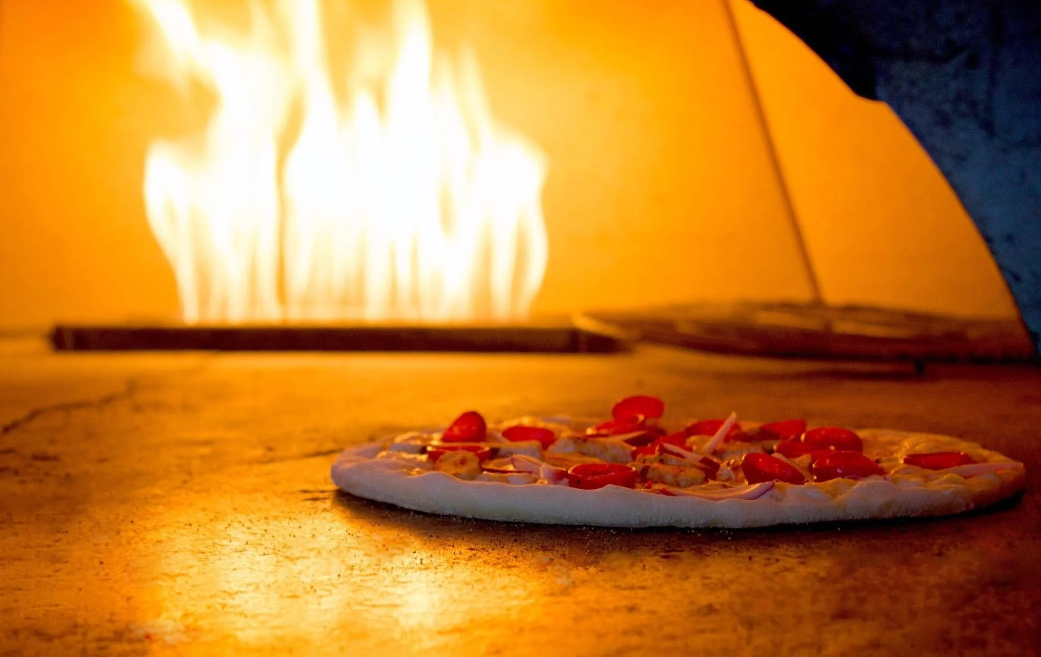 New York-style pizza baking in a brick oven with bright flames creating a crisp, foldable crust.