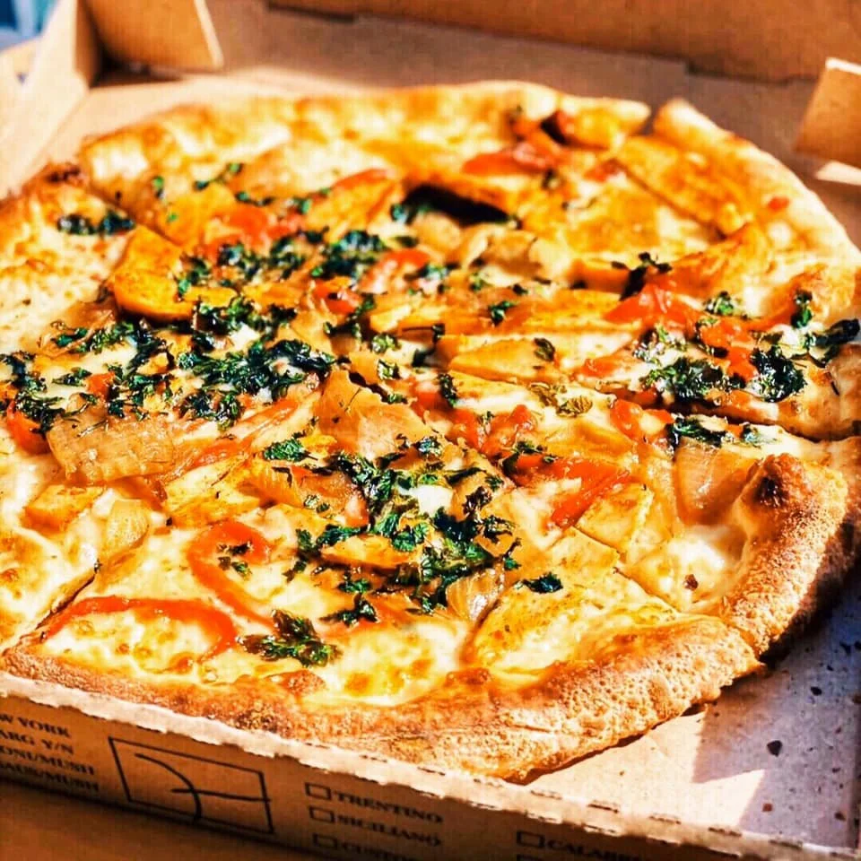 Close-up of an unbaked Amici’s half-baked pizza topped with roasted vegetables and herbs.