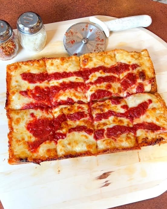 Three Cheese Red Top Vegetarian Detroit-style pizza featuring crispy cheese edges, striped tomato sauce, and a thick rectangular crust, served with a pizza cutter and condiment jars.