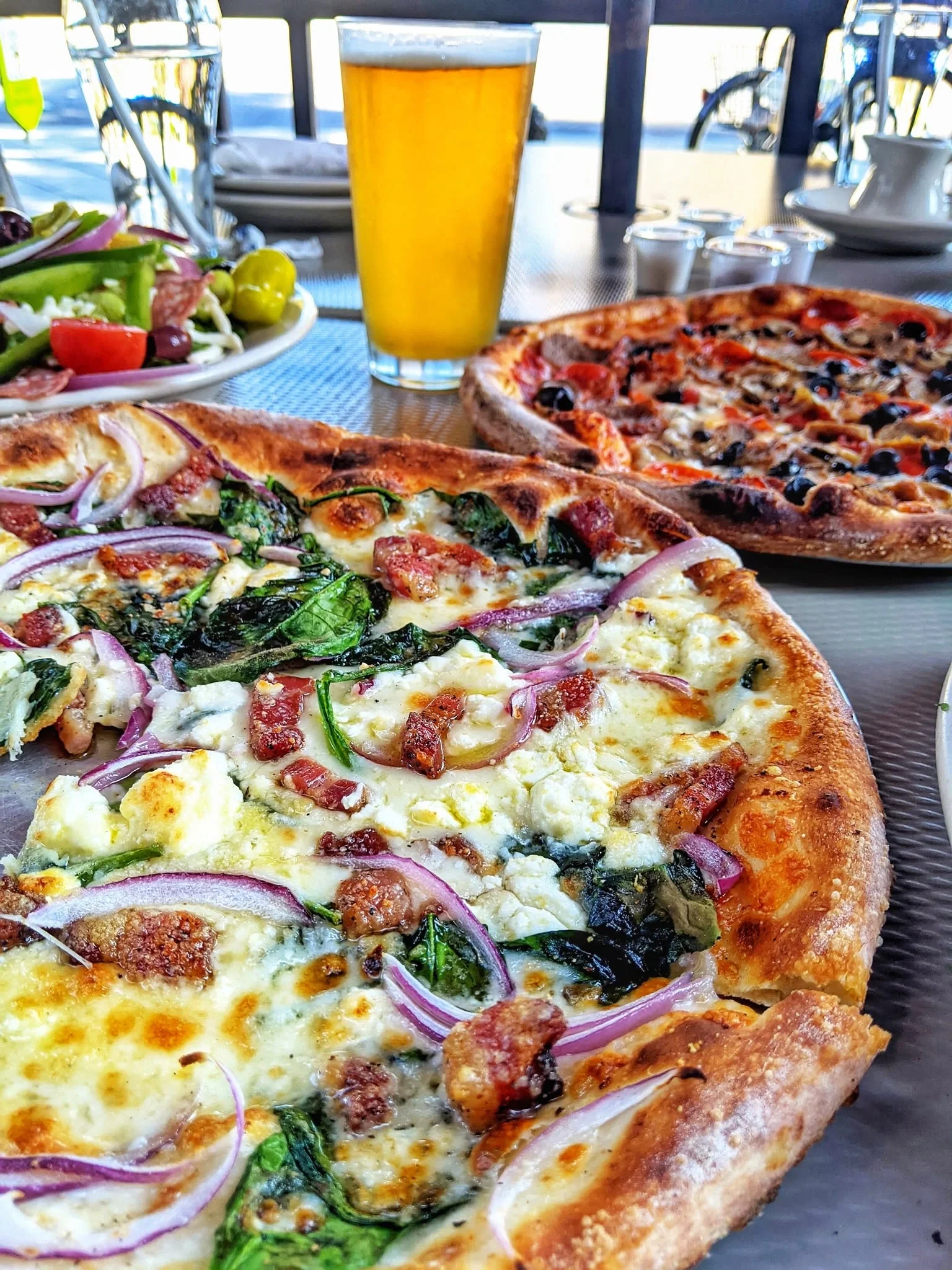 Amici's Trentino pizza and Amici's Combo pizza served with fresh salad and beer on a restaurant table.