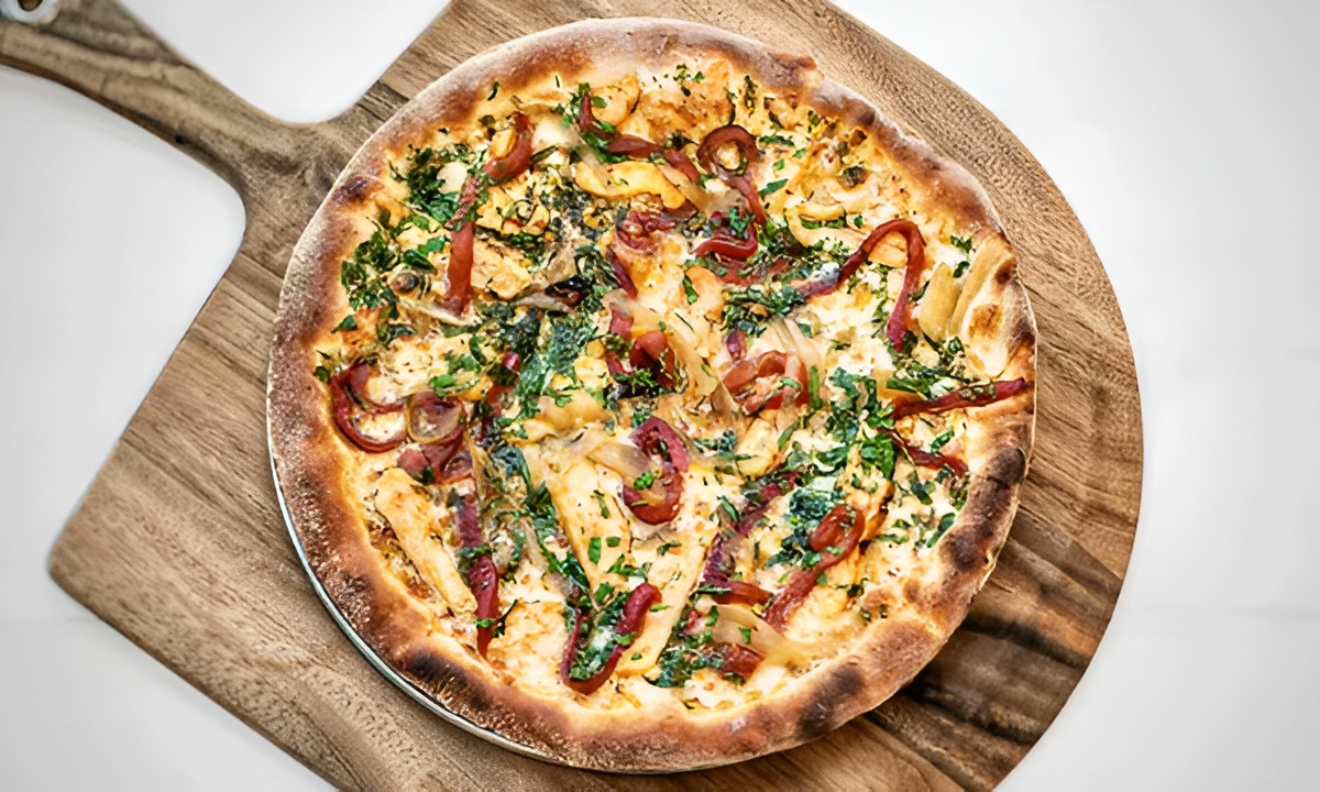 Amici’s gluten-free spicy pepper chicken pizza with roasted peppers and onions on a wooden peel.