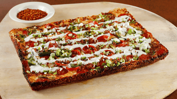 Firehouse Special Detroit-style pizza topped with veggies and a bowl of chili flakes at Amici’s.