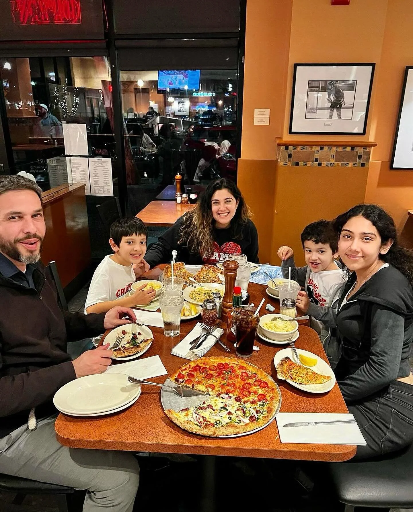 A family of five eating pizzas and Italian dishes at Amici’s East Coast Pizzeria.