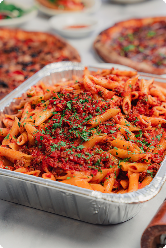 A table filled with Italian food from Amici’s, including pasta dishes, fresh salad, and brick-oven pizzas in a casual dining setting.