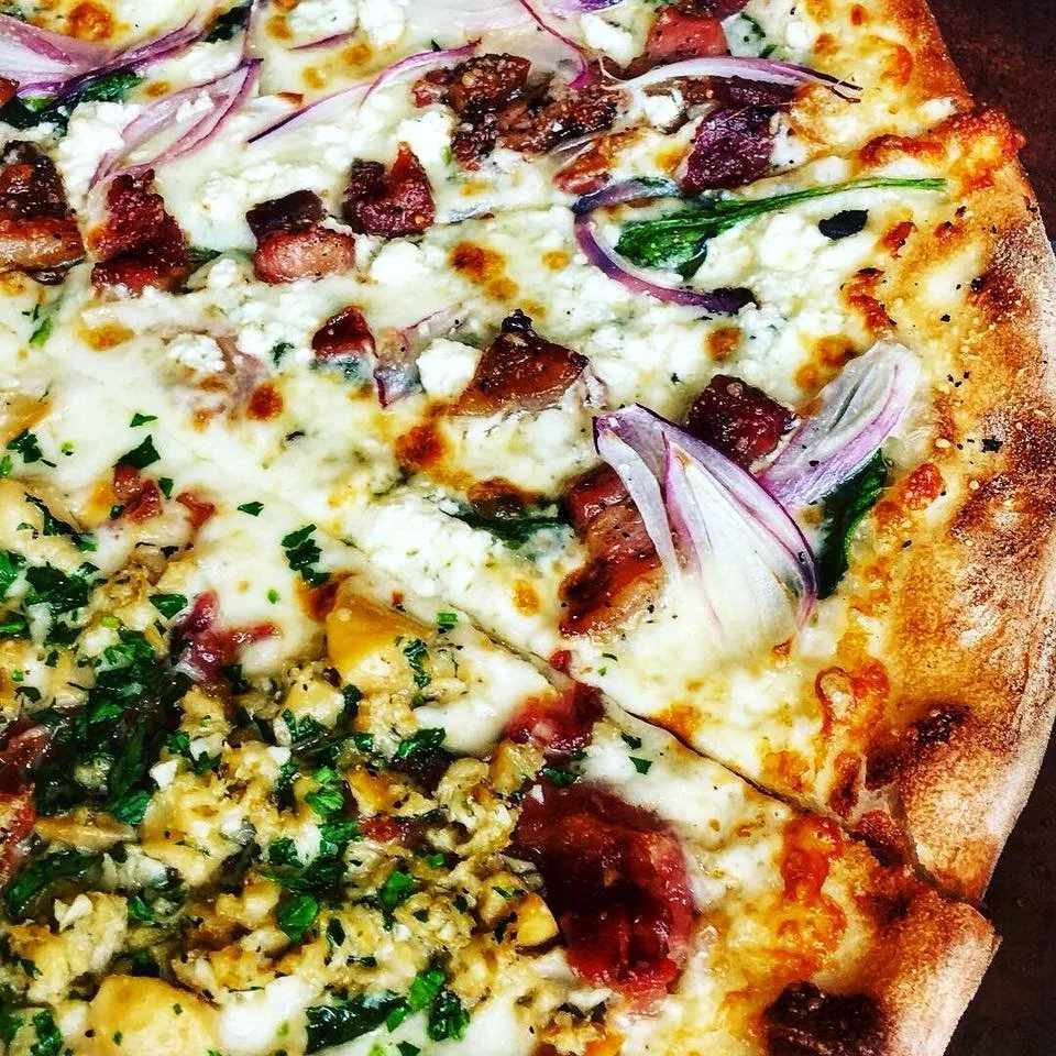 Half-and-half Amici’s pizza featuring White Clam and Trentino toppings with melted cheese and fresh herbs.