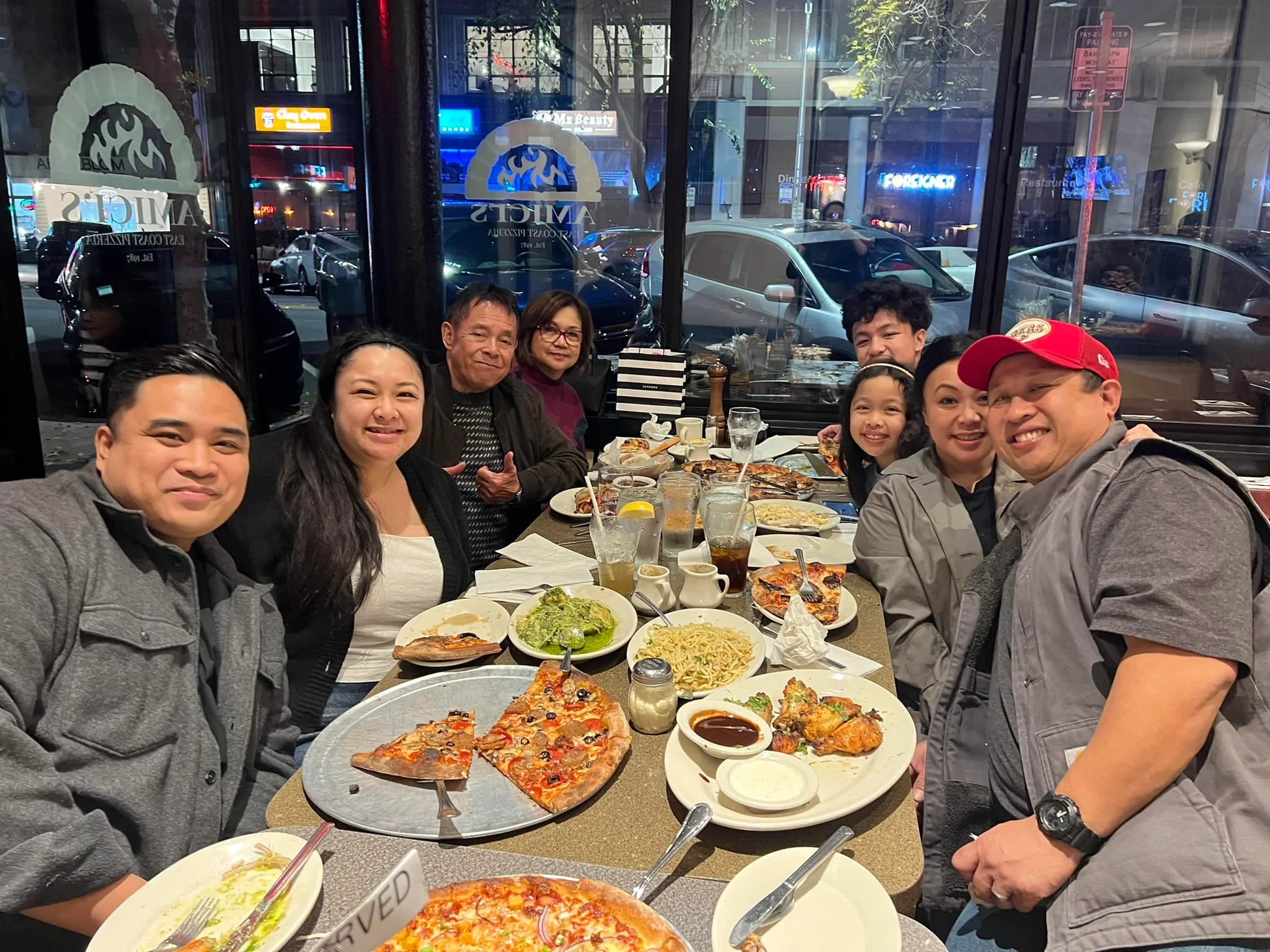A family of eight enjoying their dinner of pizza, sides, and cool drinks at Amici’s East Coast Pizzeria.