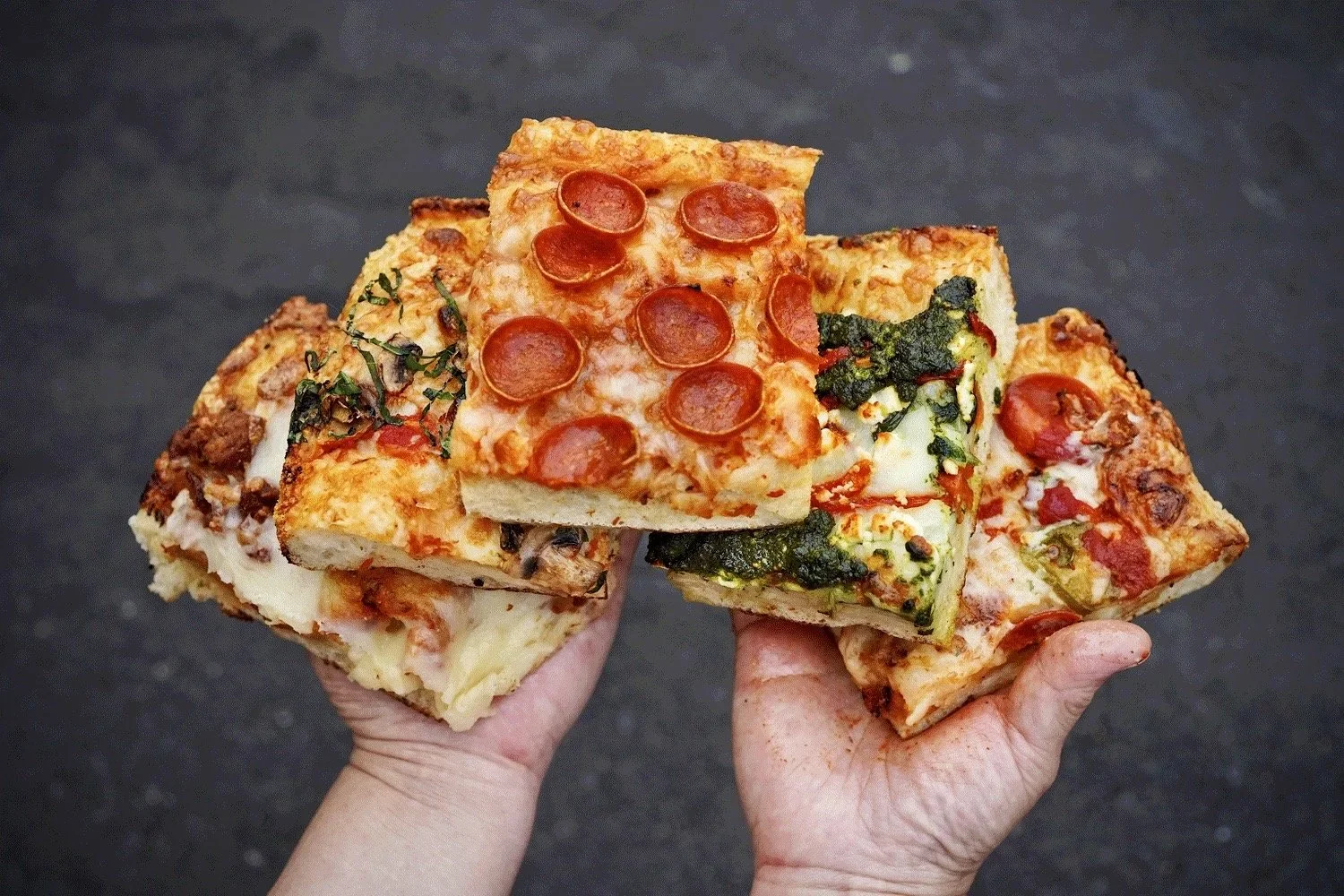 A person holds five unique flavored Detroit-style pizzas from Amici’s.