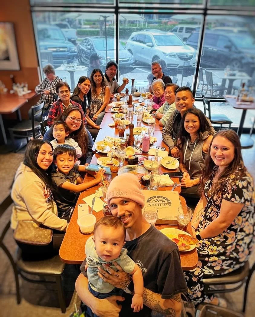 A large group enjoying pizza, pasta, drinks, and shared plates at a long table catered by Amici’s.