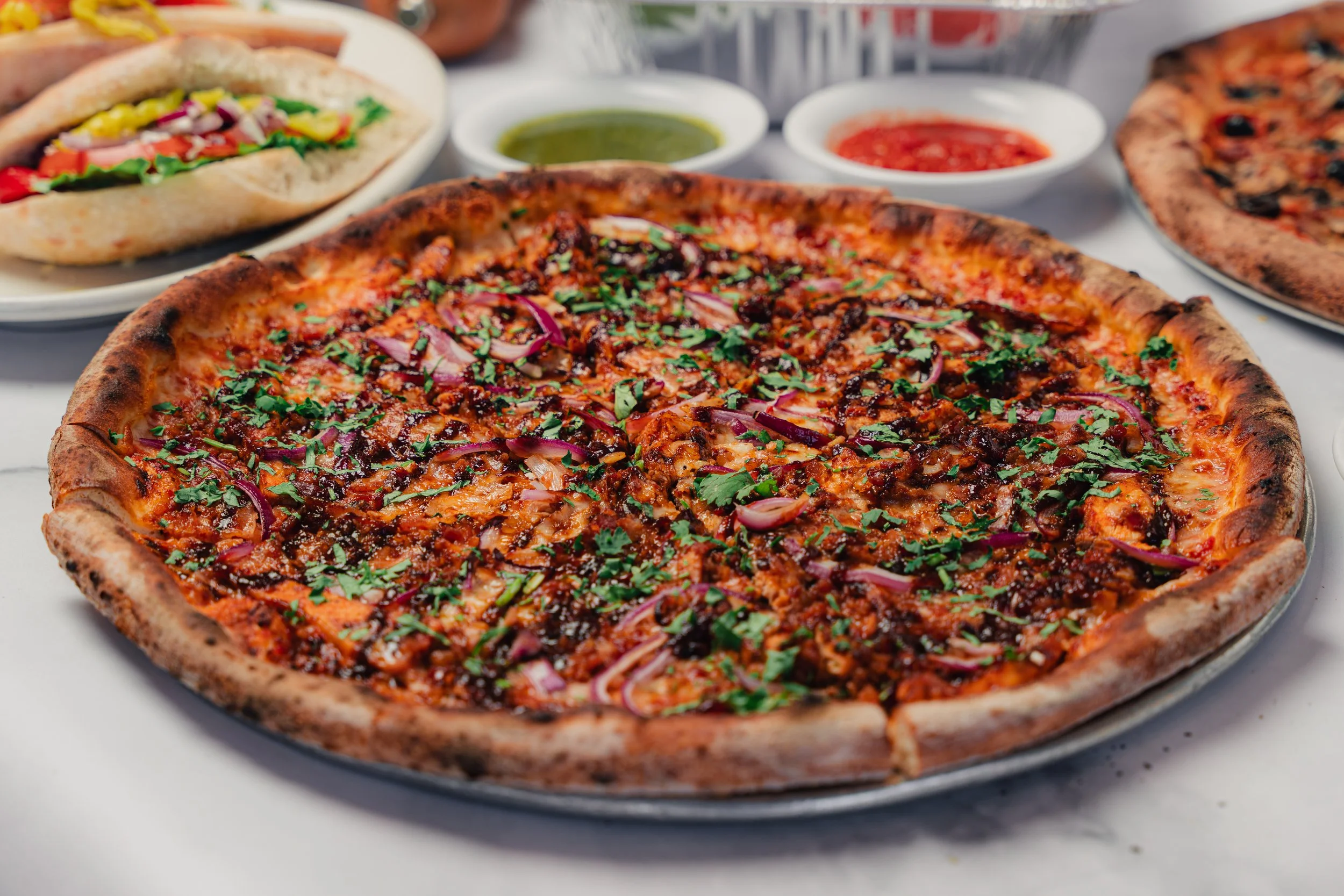 BBQ chicken pizza and a sandwich arranged on a table, featuring a casual takeout meal setup.