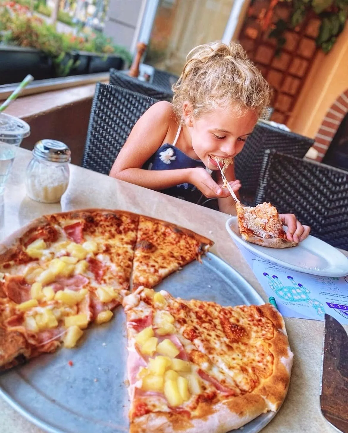 Young girl smiling as she stretches melted cheese from a slice of Amici's New York-style cheese pizza.