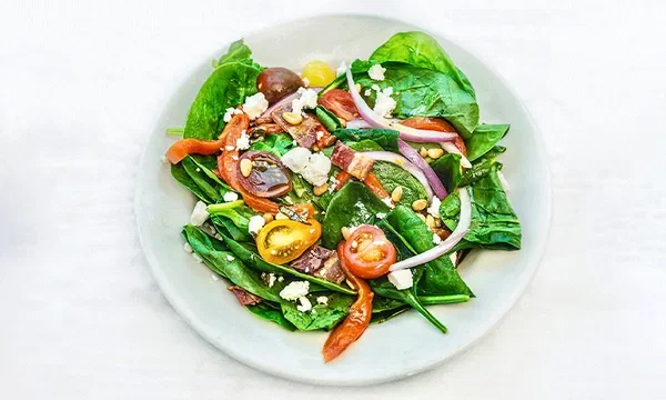 Amici’s Spinach Salad with roasted red peppers, red onion, tomato, bacon, crumbled feta, and toasted pine nuts.