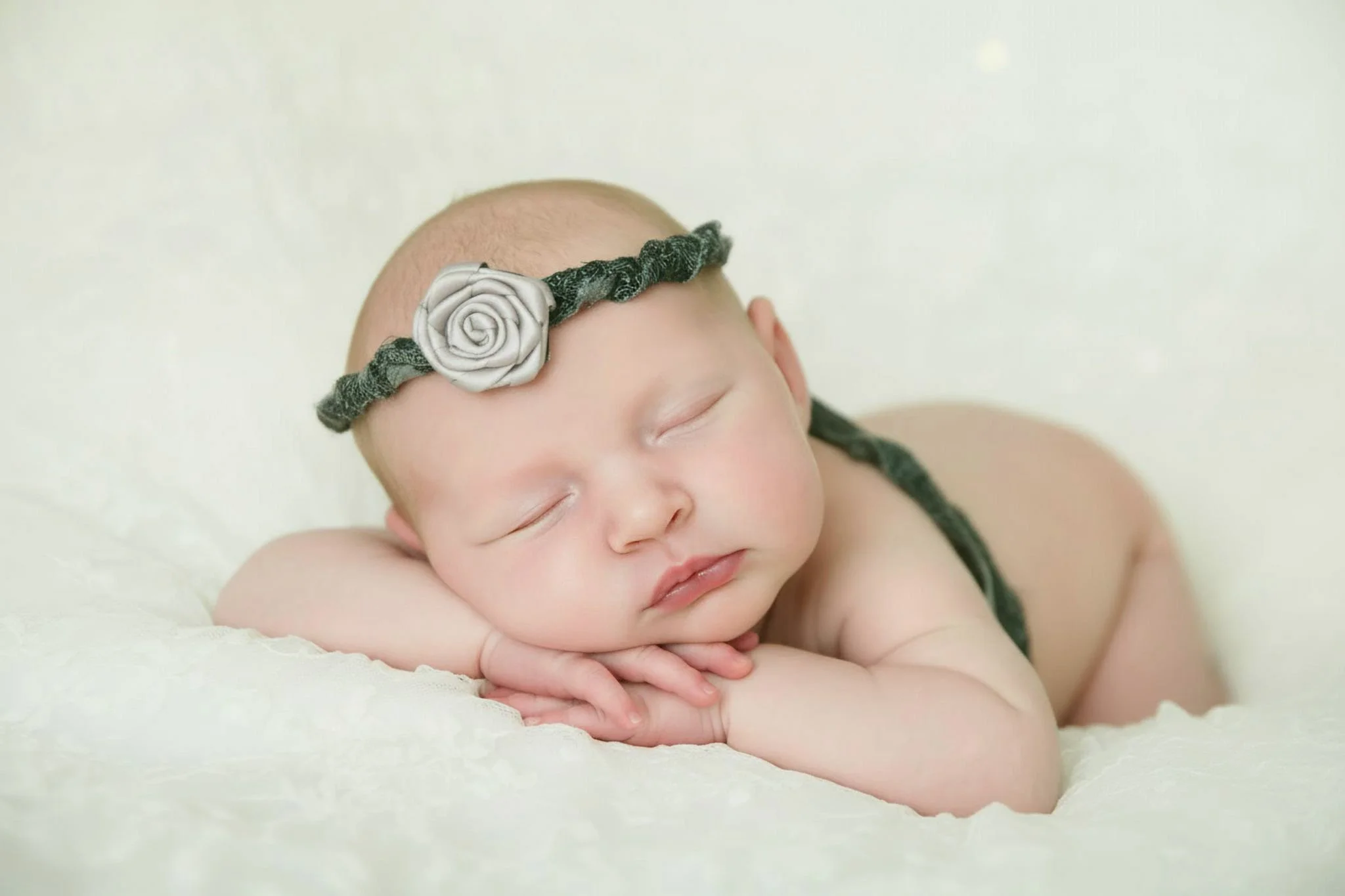 Omaha Newborn Photographer posed baby sleeping on stomach with just a headband on folded little hands 