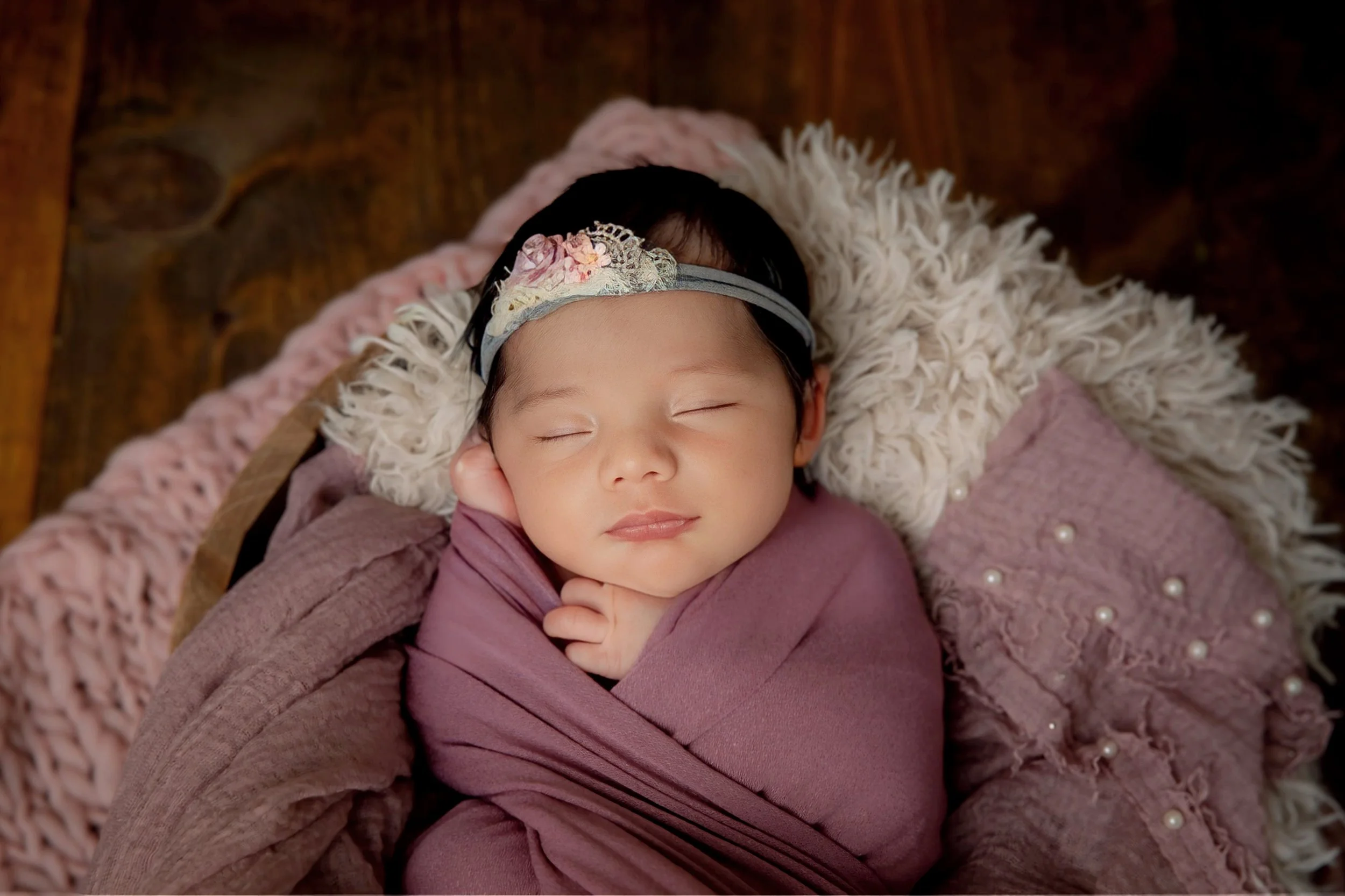 Omaha Newborn Photographer in studio with newborn girl wrapped in purple tones and sleeping 