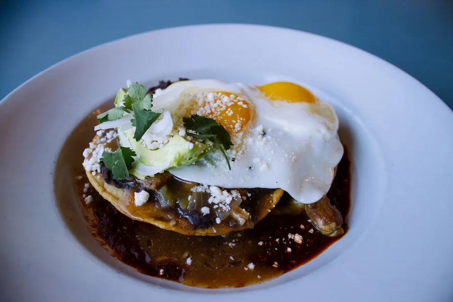 Huevos Rancheros: crispy corn tortillas, refried black beans, salsa roja, green chile stew, Cotija cheese, avocado, 2 sunny side eggs*.