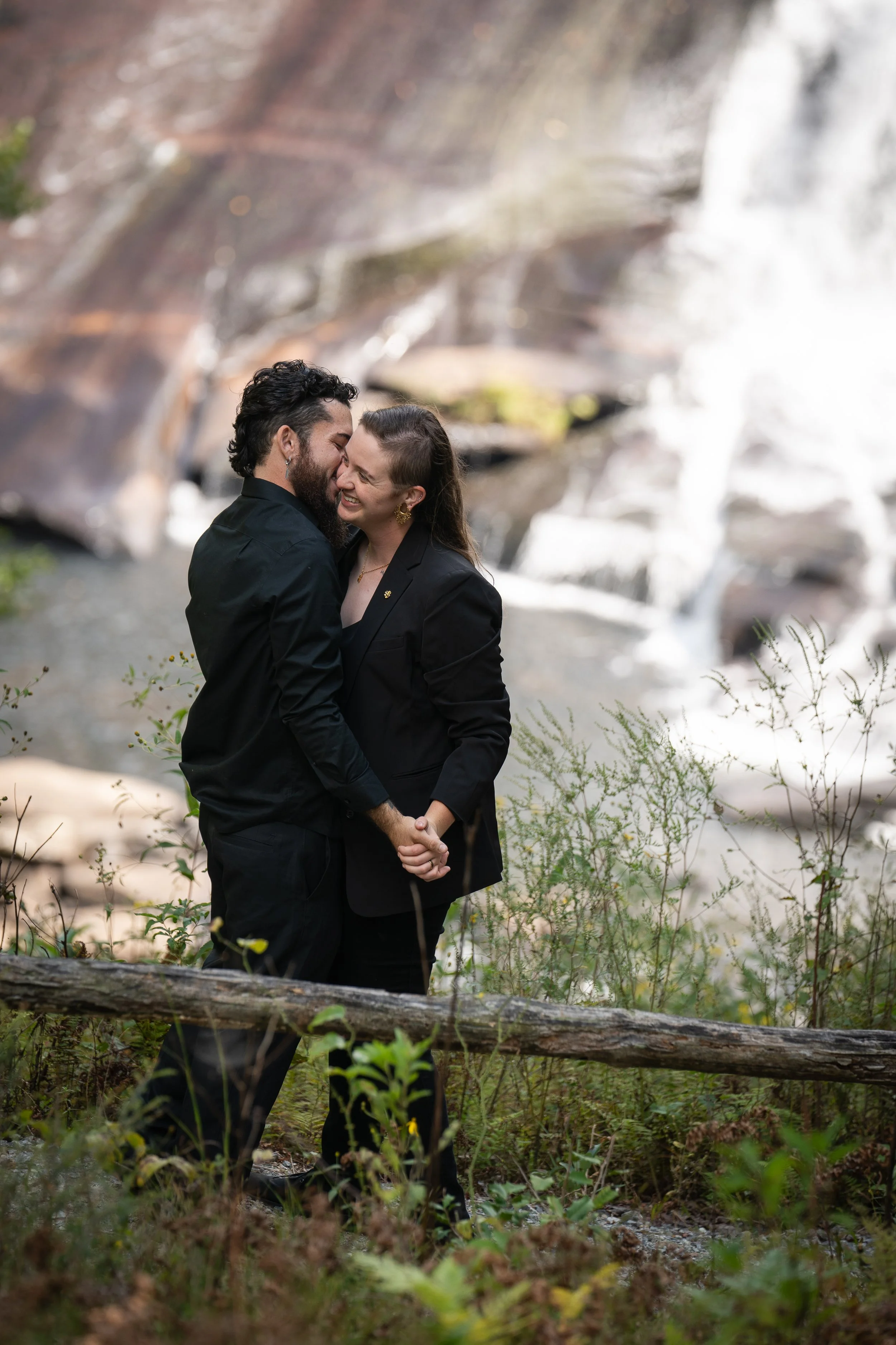Glowing couple in love, embracing in front of a waterfall.