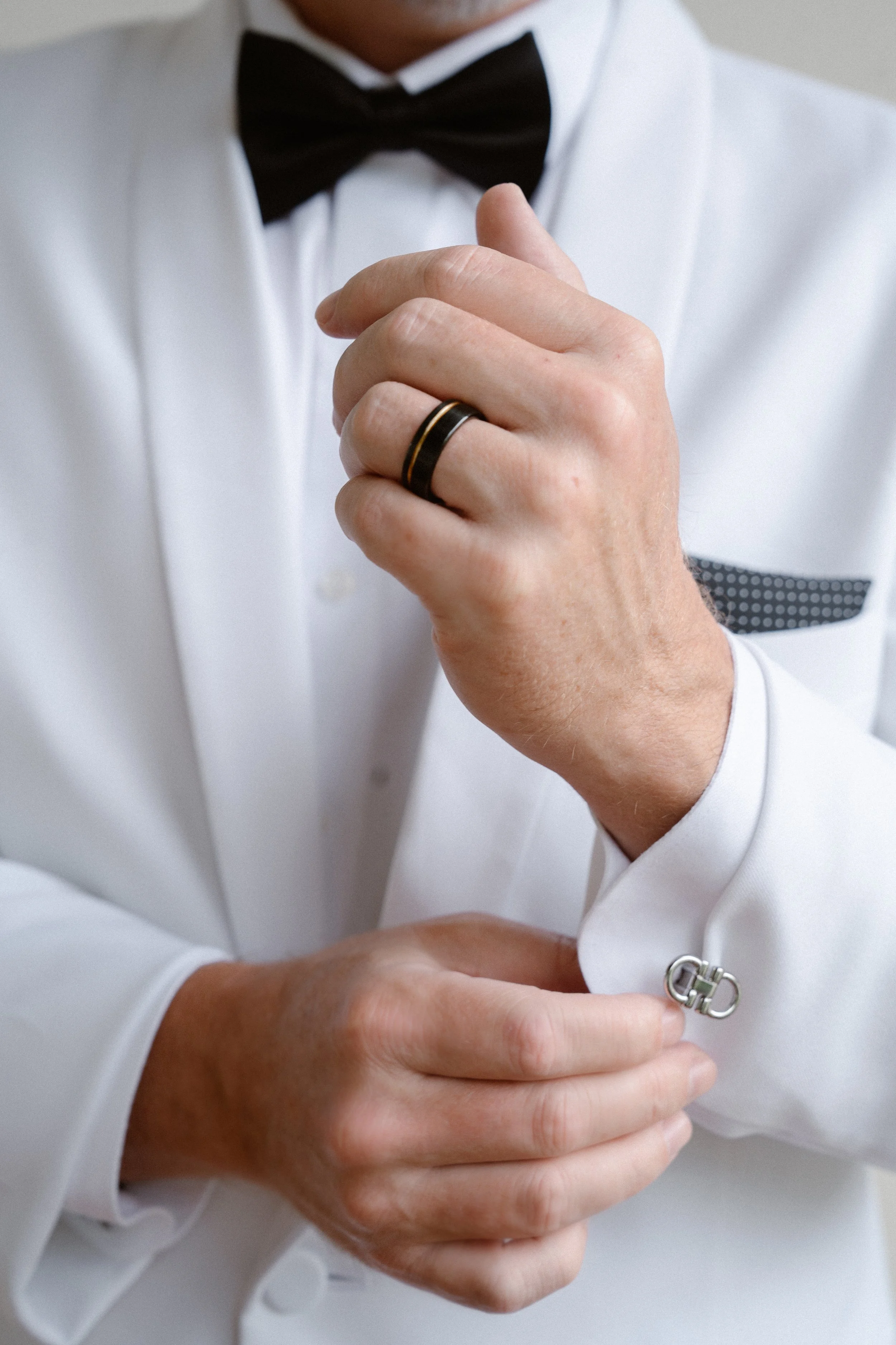 A groom sharply dressed in a white tuxedo, straightens his personalized cufflinks.