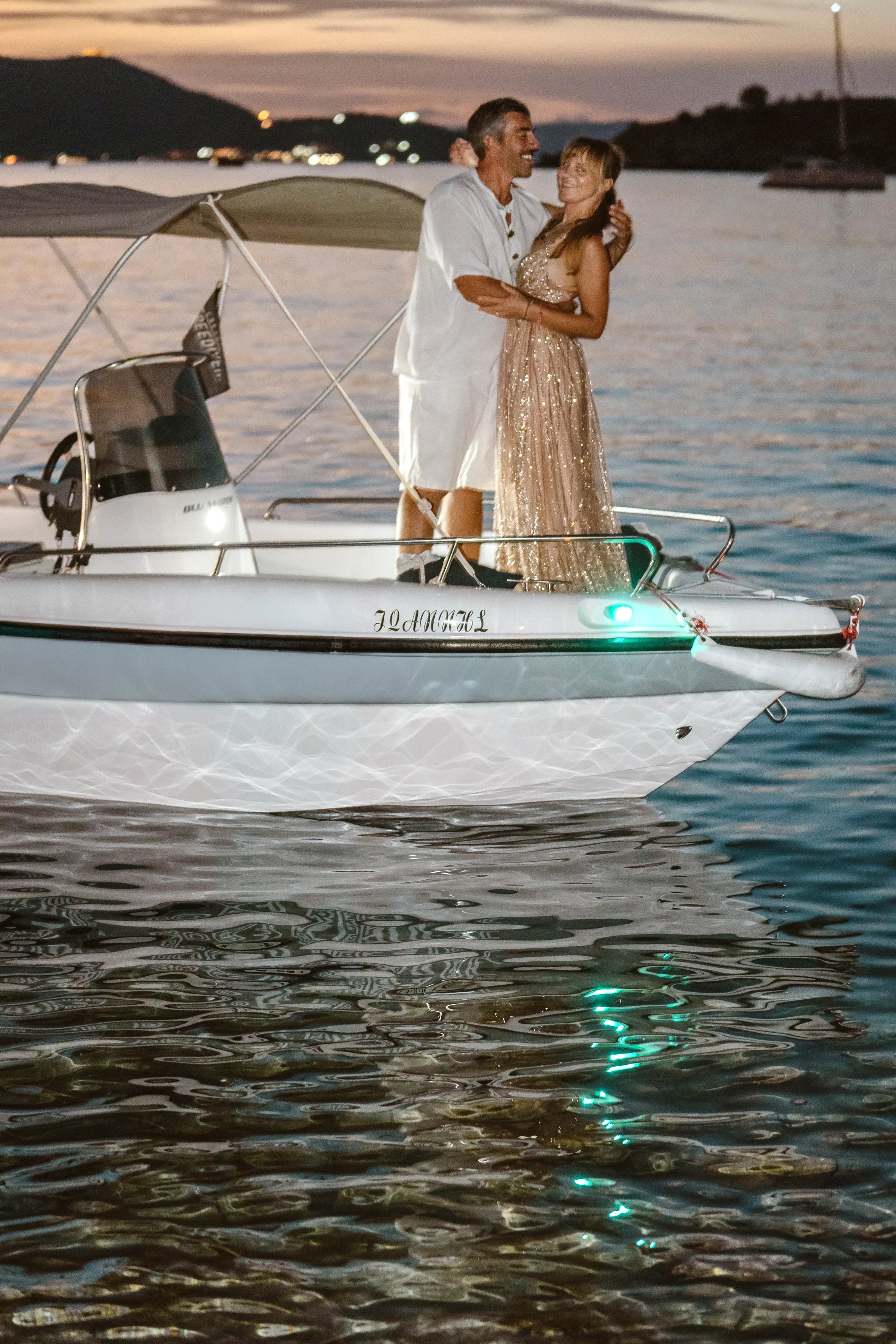 Newly eloped couple embrace at dusk on their private boat in a small harbor on the Northern Cretan coast.