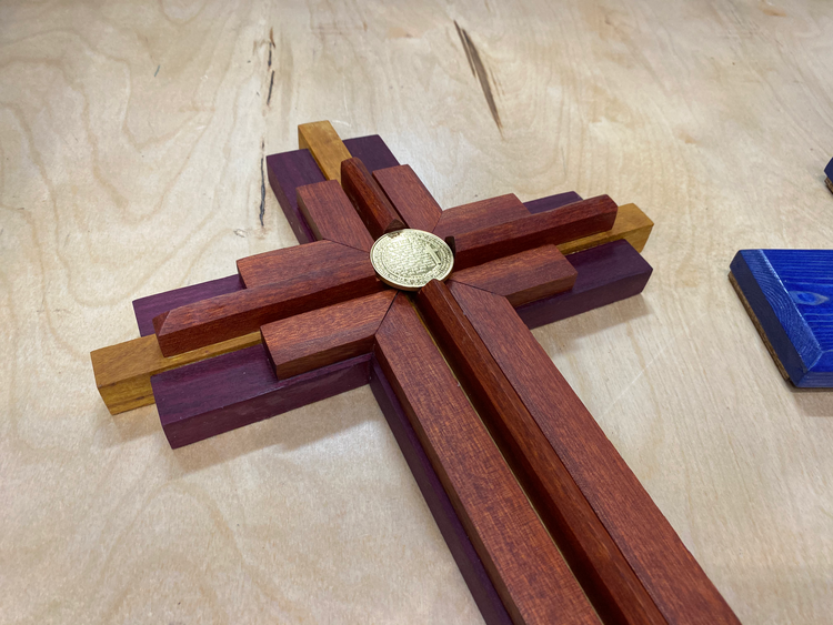 Layered wooden cross stained red, white, and blue with an embedded coin
