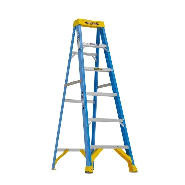 Werner FS100CZ 6 foot fiberglass step ladder featuring a yellow frame and integrated tool storage top standing inside a workshop
