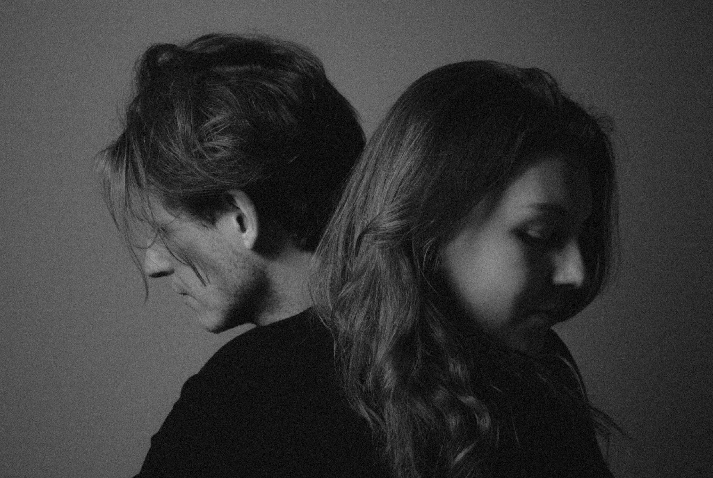 A black-and-white image of two women standing back to back with their heads touching, sharing a moment of closeness.