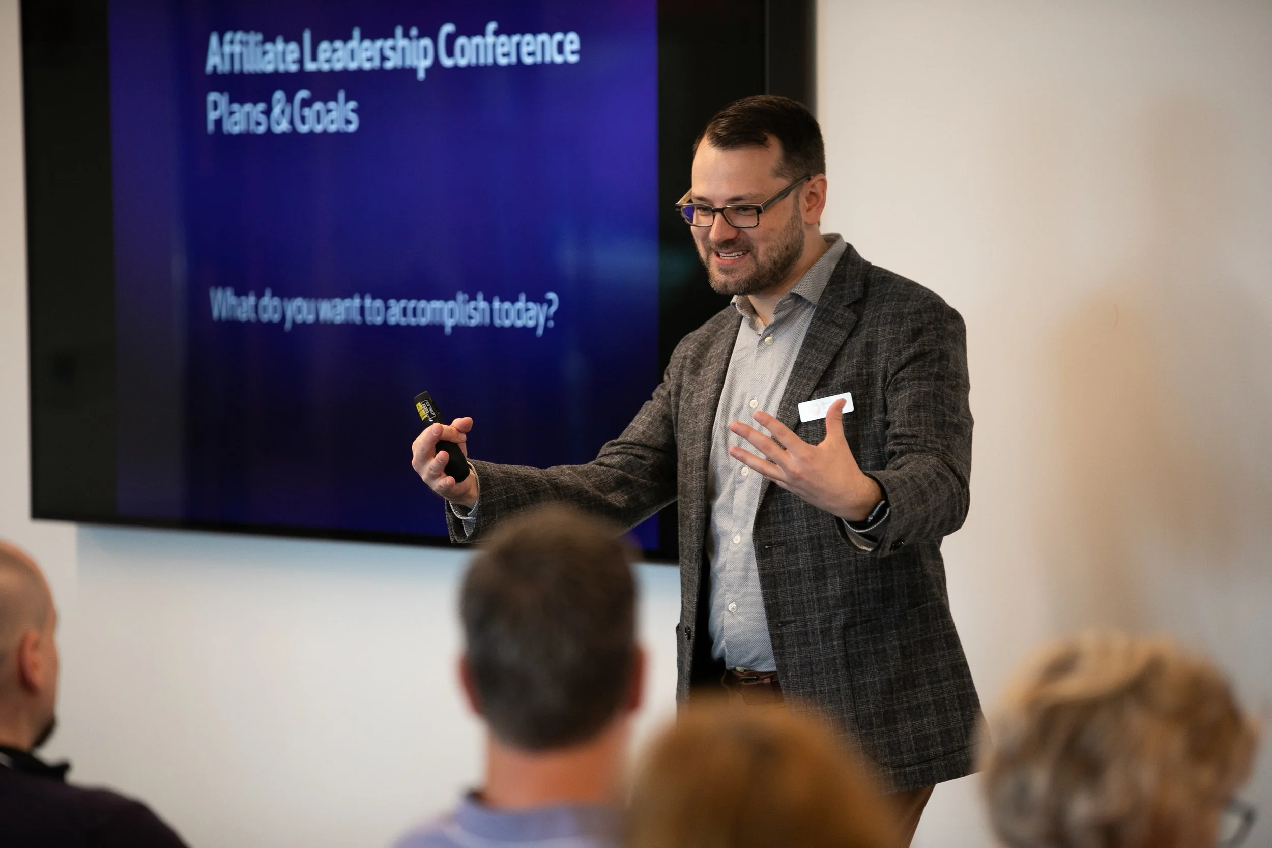A man leads an engaging discussion with partners of the Scholastic Awards in a conference room. A screen behind him reads "Affiliate Leadership Conference Plans & Goals."