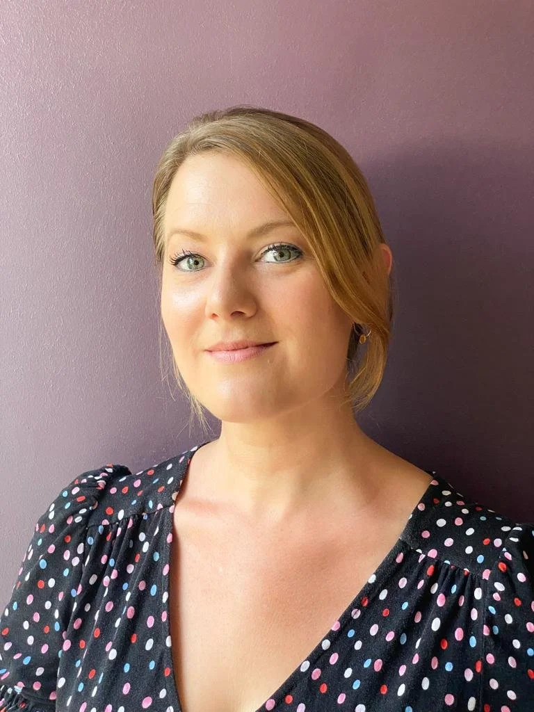 Dr Holly Powell-Jones - a blonde woman in her 30s, photographed head and shoulders with a purple backdrop