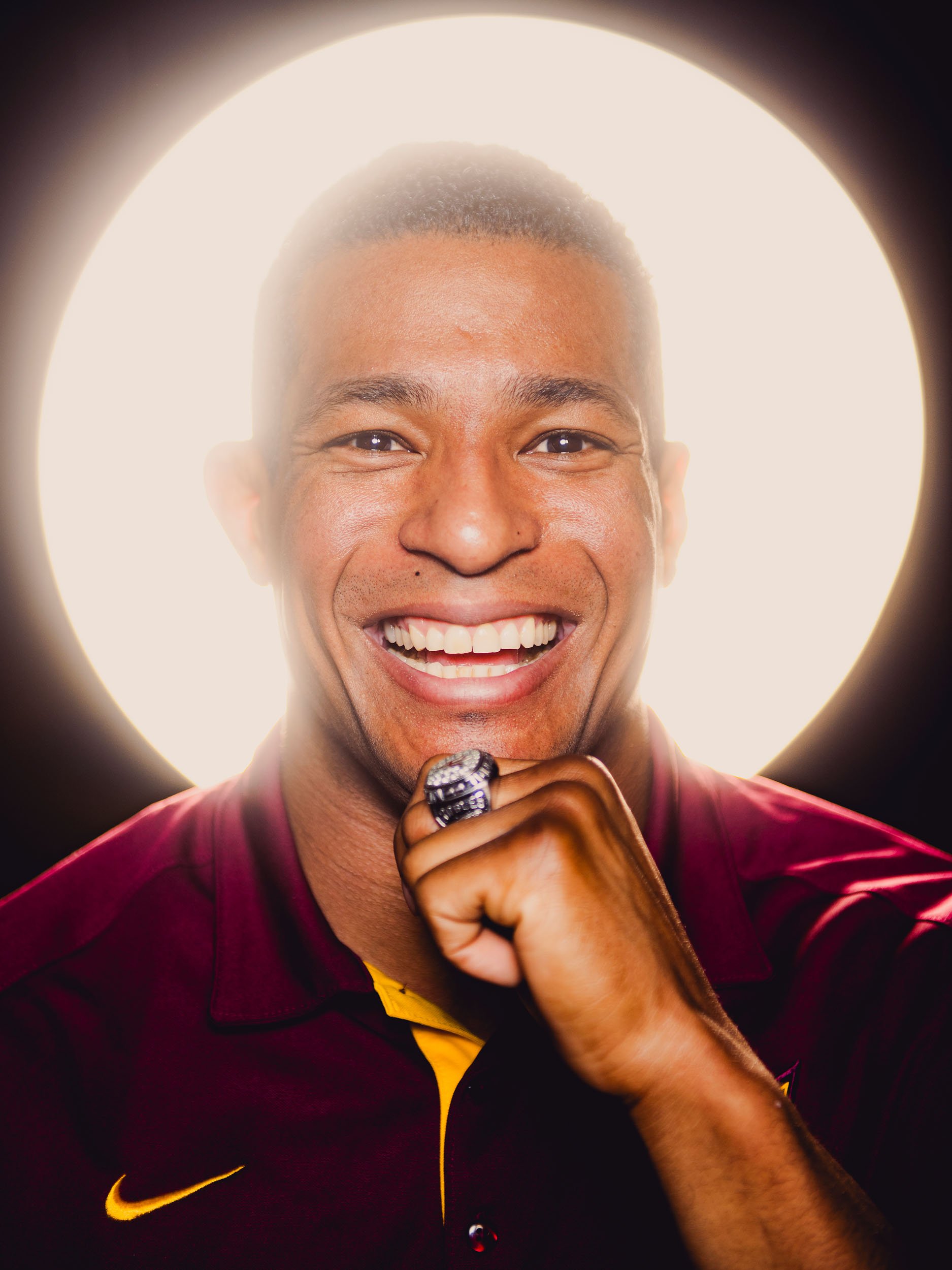 ASU Athlete Anthony Robles in maroon Nike shirt with championship ring, backlit by bright circle, a studio brand portrait  for Sun Devil Athletics in Tempe, Arizona.