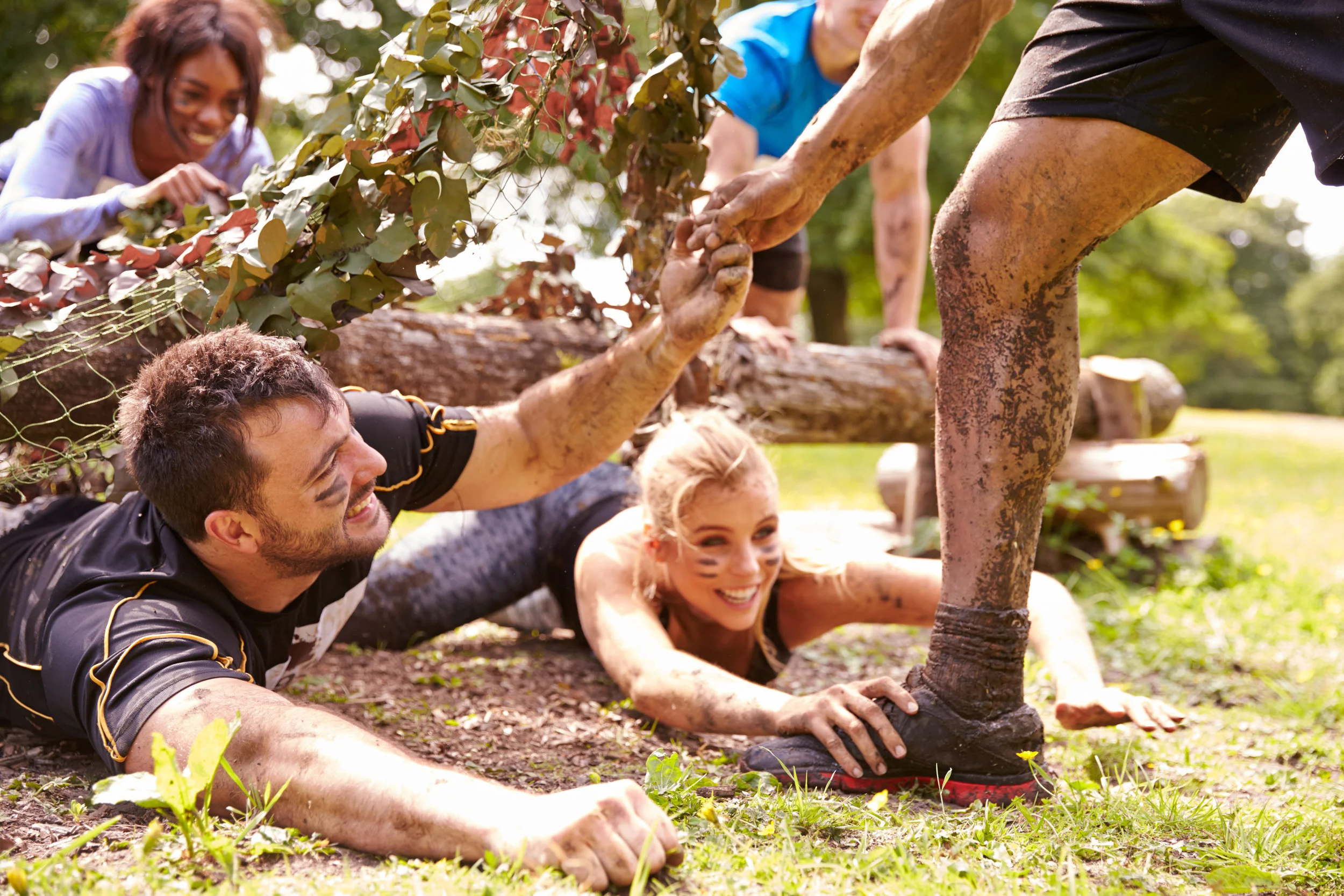 Assault course competitor helping others crawl under nets