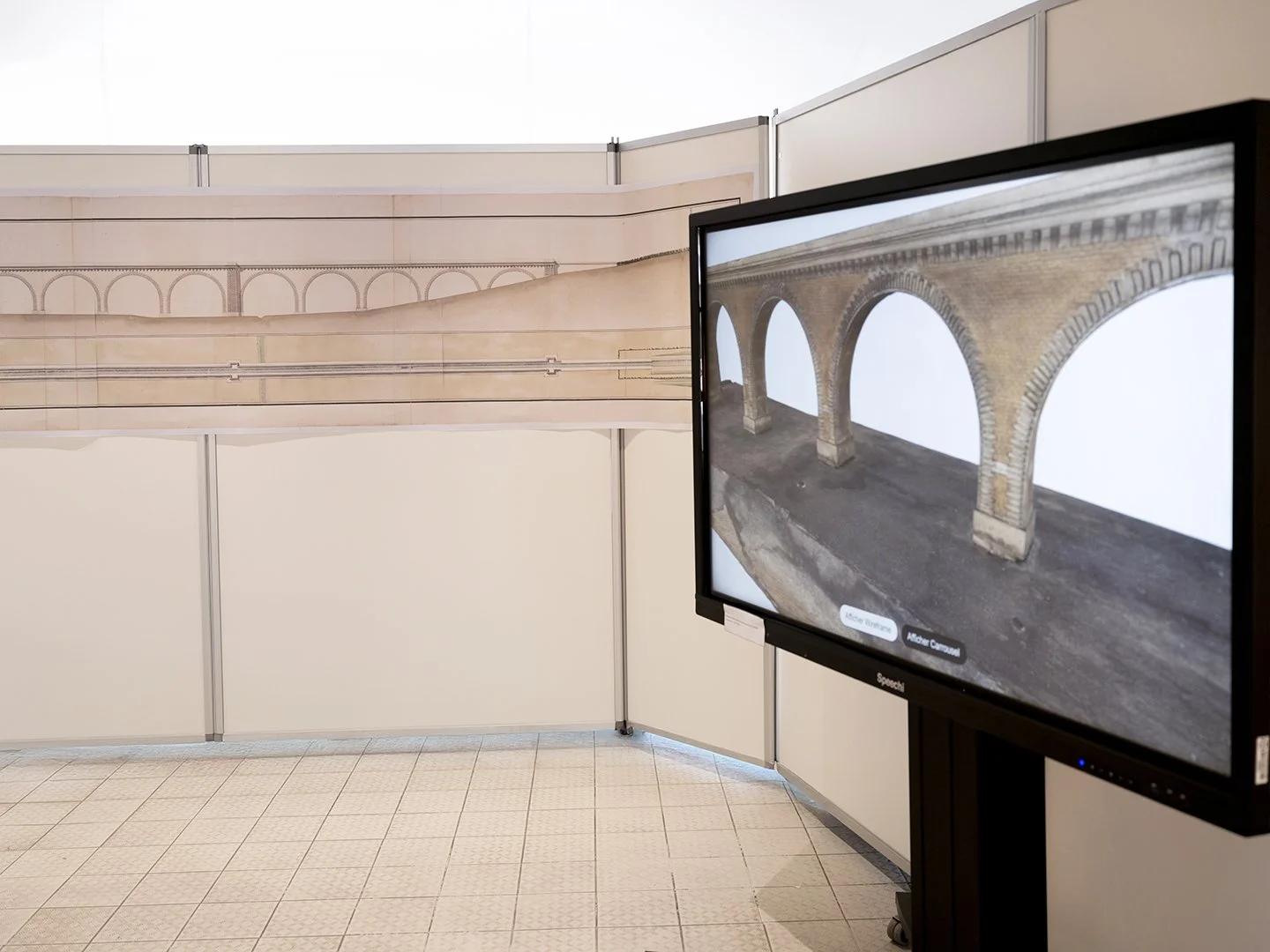 Espace d’exposition avec un long dessin technique de pont accroché au mur et, à droite, un écran montrant une modélisation 3D d’arches en pierre, illustrant l’analyse architecturale de l’ouvrage.