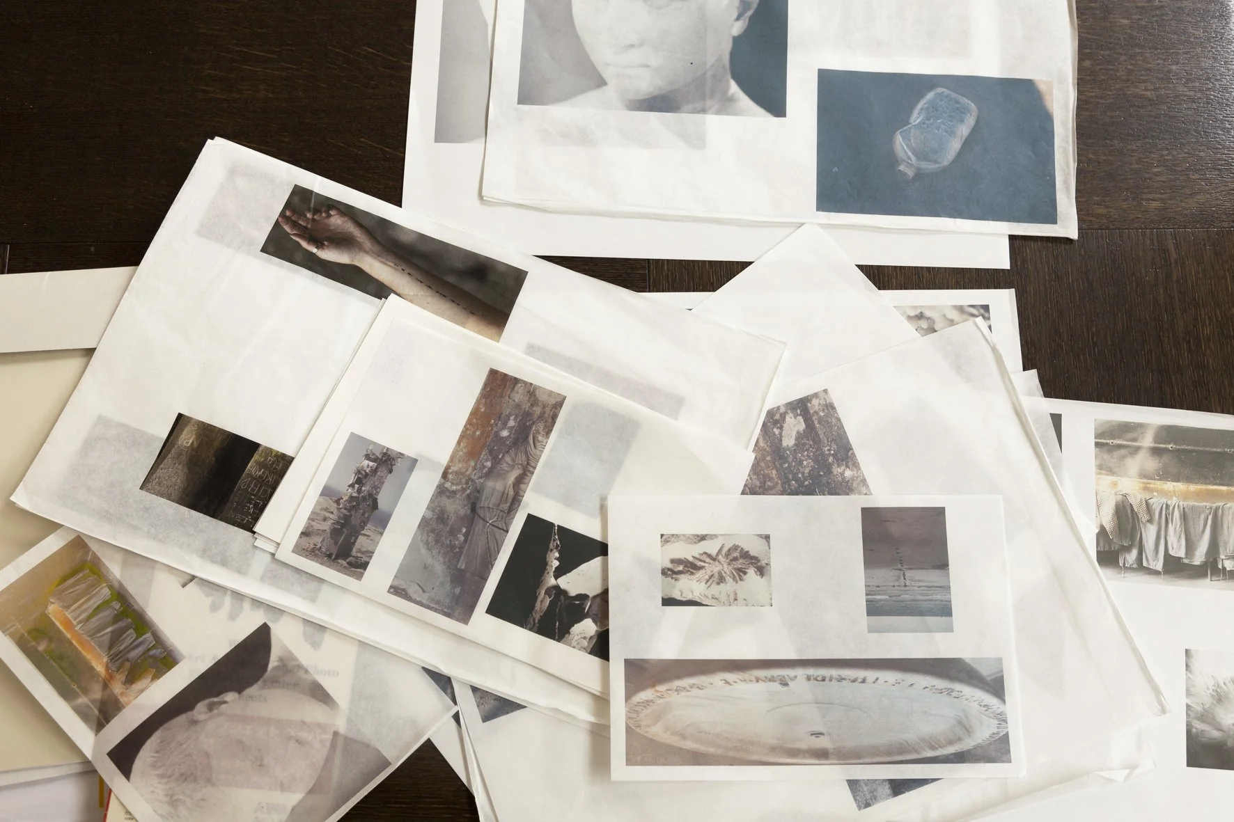 Feuilles de papier superposées sur une table en bois, couvertes d’images imprimées : fragments de corps, visages, paysages, objets et textures. L’ensemble évoque un travail de recherche visuelle ou un montage artistique en cours.
