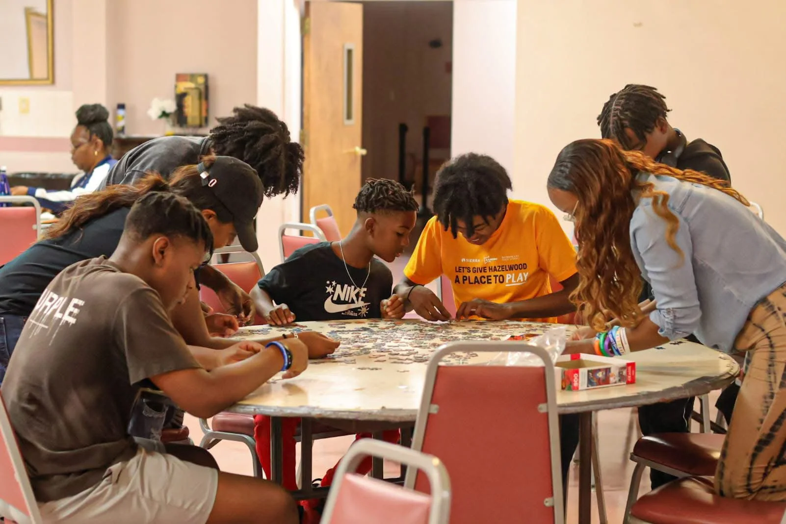Group of young people gathered around a large table working on a puzzle together.
